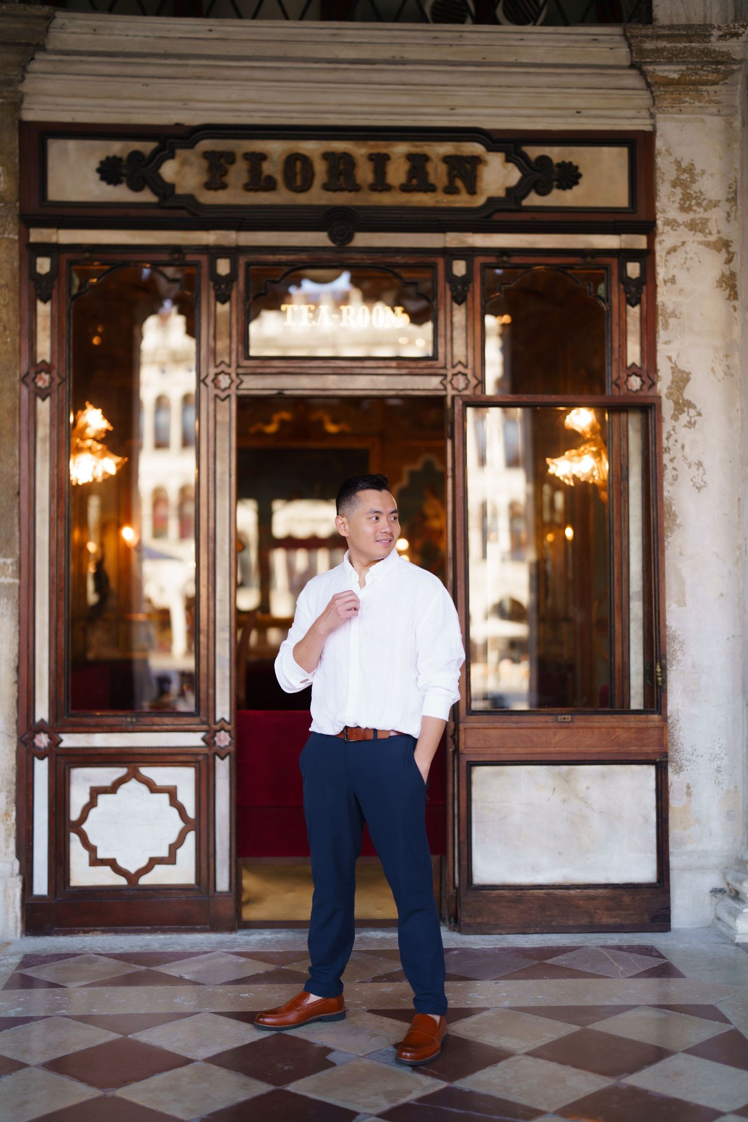 Man in white shirt and navy pants poses confidently outside Caffe Florian in Venice, Italy.