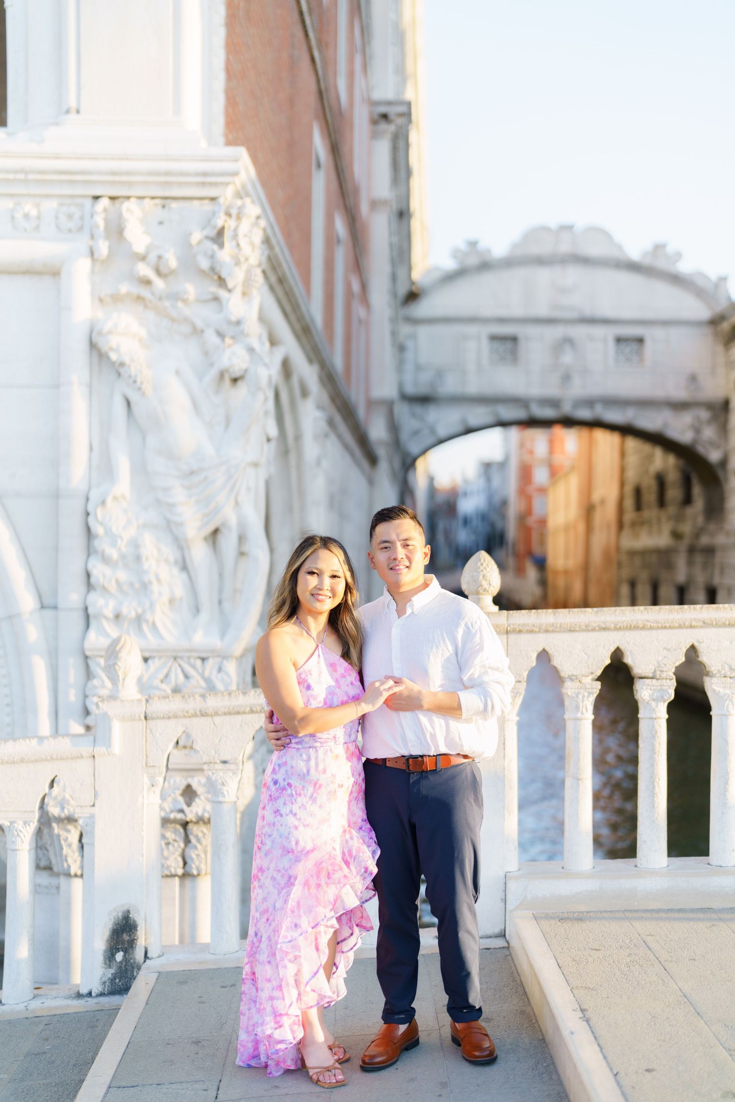 Couple posing together on a bridge in Venice, Italy, with the Bridge of Sighs visible in the background.