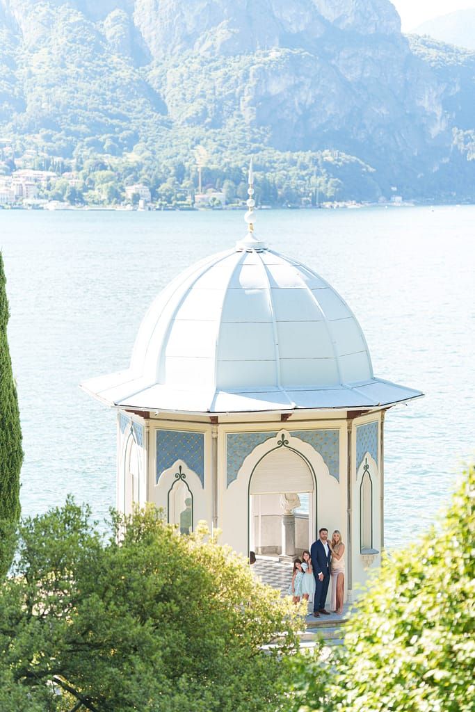 Elegant white domed gazebo overlooking Lake Como in Italy with mountains and cypress trees in the background.