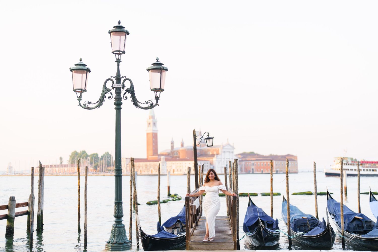 Covered gondolas float in a Venice canal with ornate lampposts and historic buildings in the background.