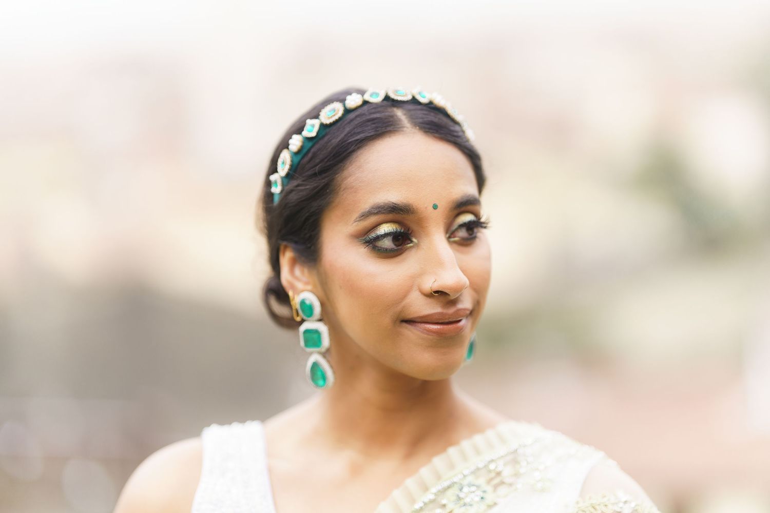 A bride in an elegant cream wedding dress and turquoise earrings poses for portraits in soft natural lighting.