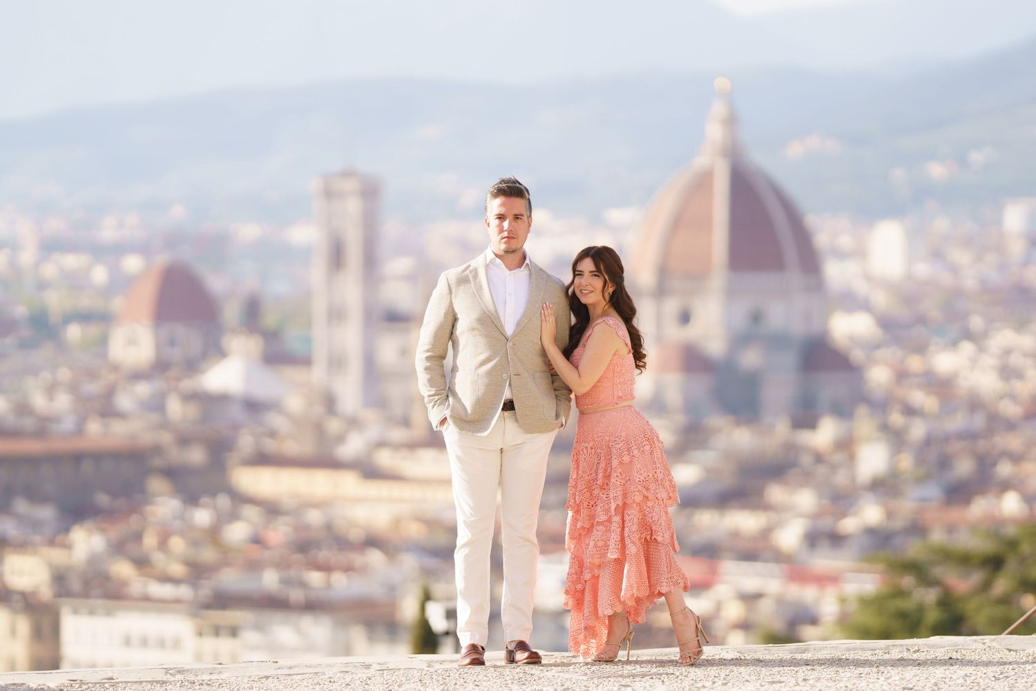 A couple in formal attire poses at scenic viewpoints overlooking Florence, Italy with the Duomo cathedral visible.