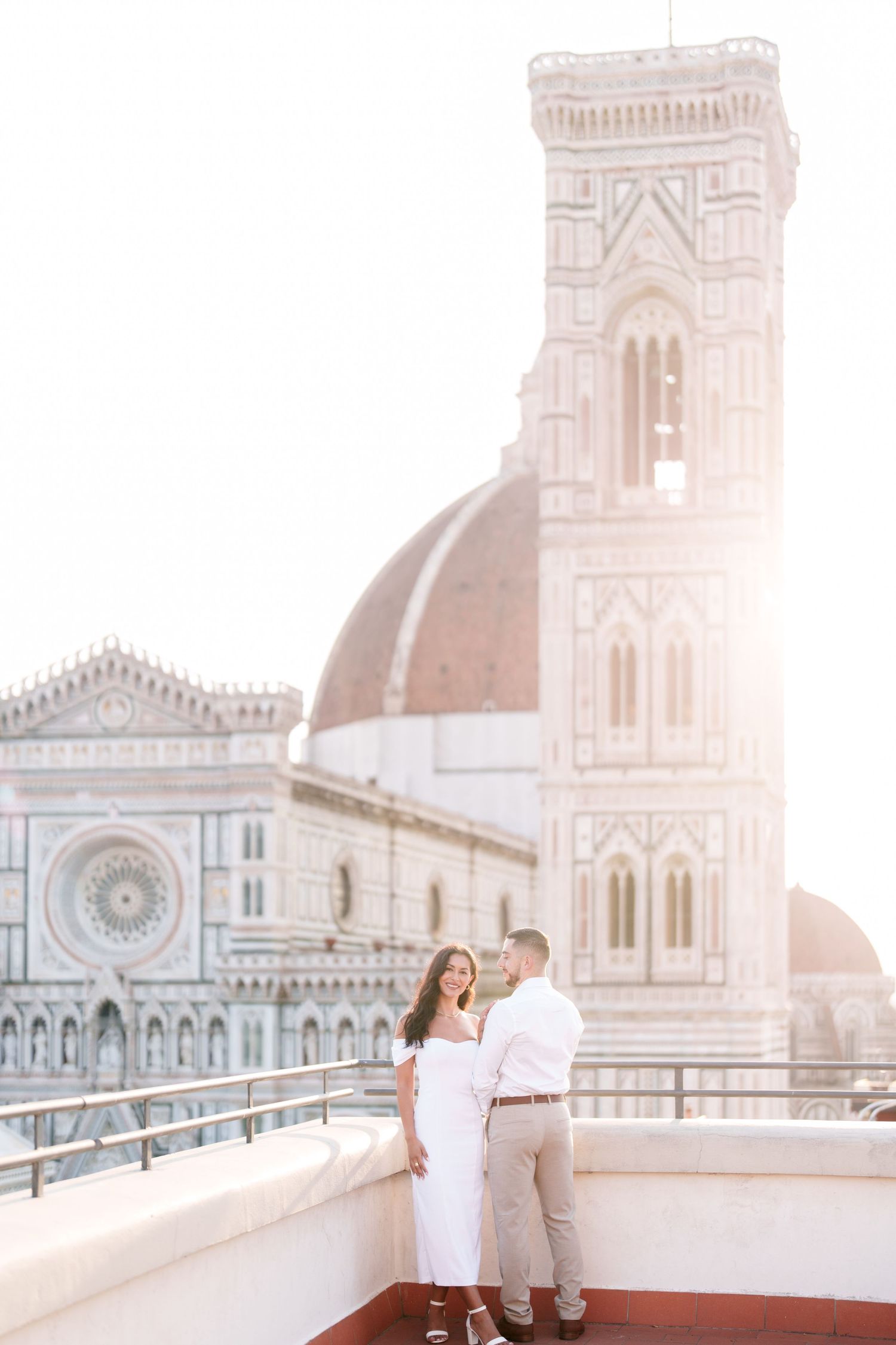 Romantic couple enjoying sunset views of Florence Cathedral's iconic dome and bell tower from a rooftop terrace in Italy.