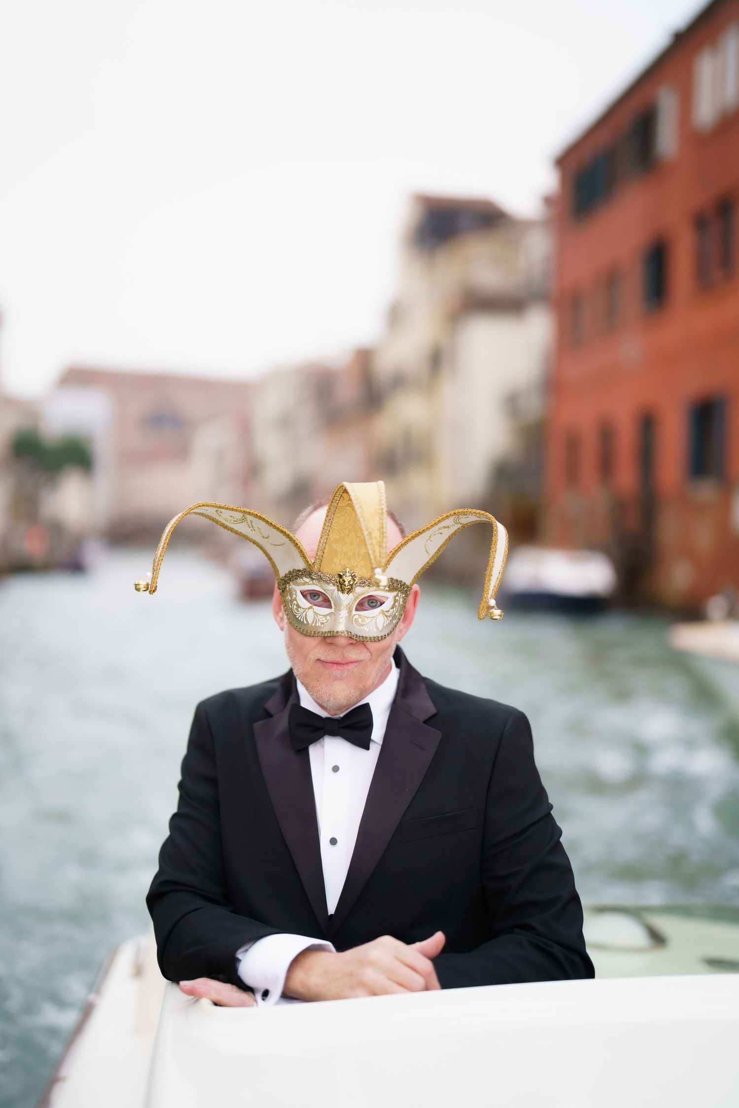 Person in formal attire and cowboy hat writes in a notebook while sitting on a boat in Venice's canals.