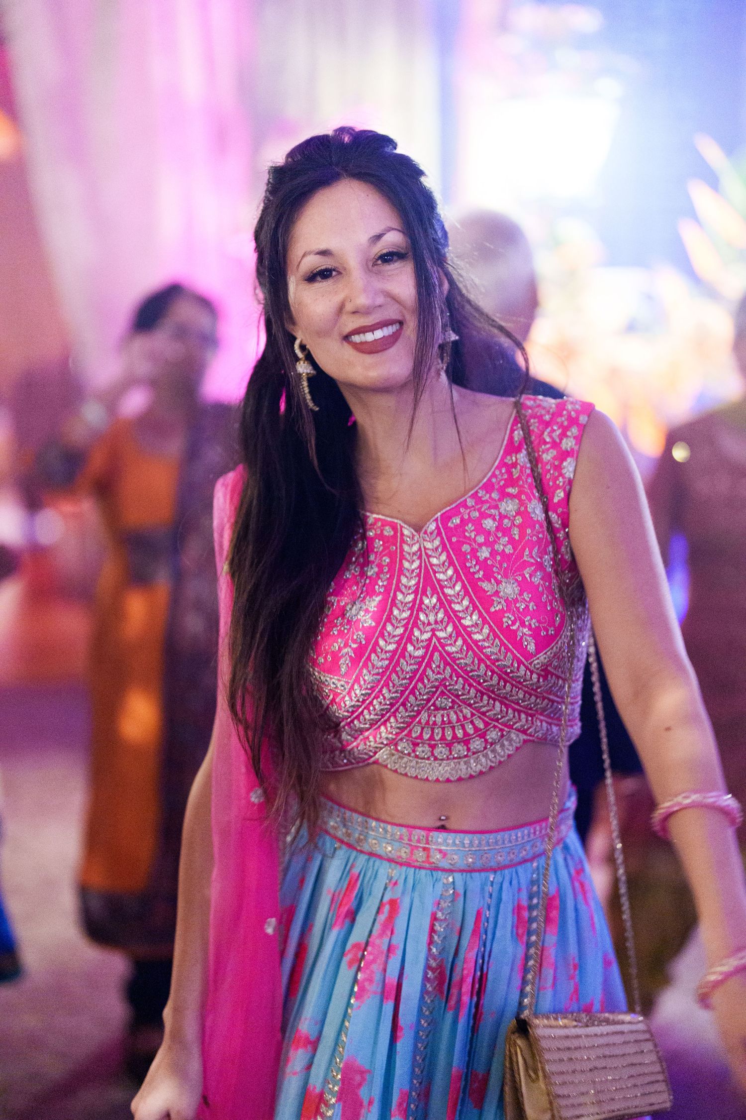 Guest in vibrant pink and blue traditional Indian lehenga dancing at a celebration.