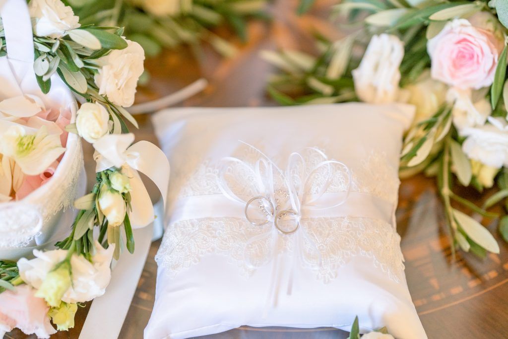 Delicate white and pink floral arrangements with greenery decorate wedding ceremony space.