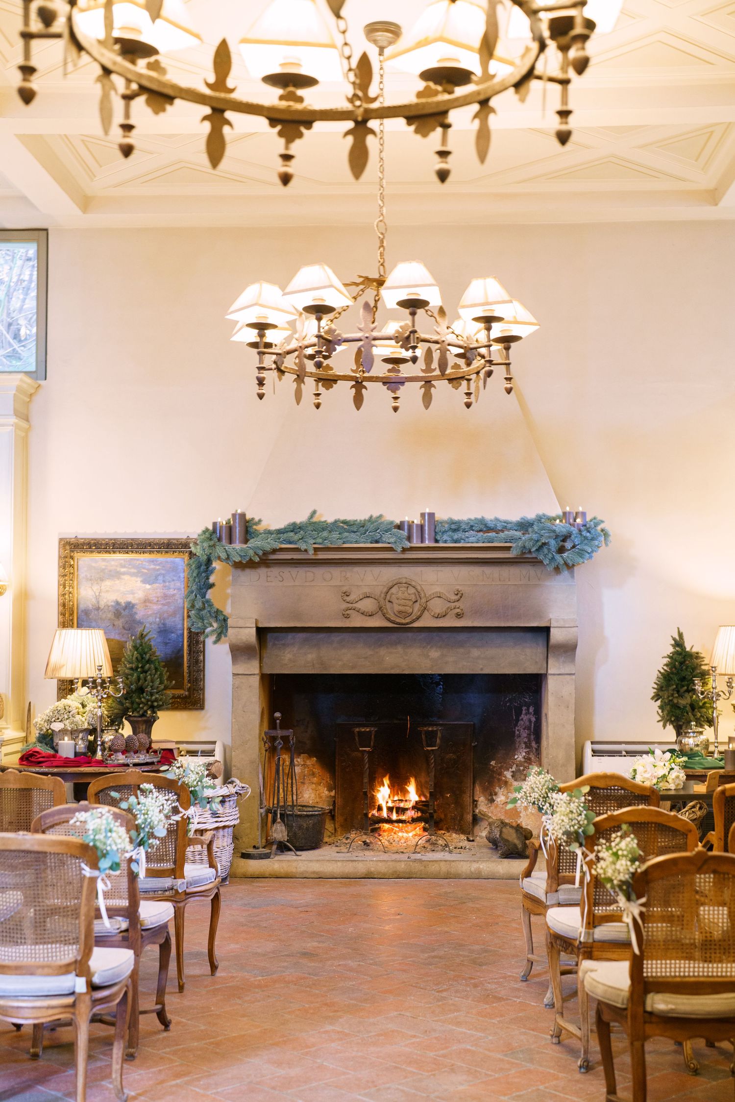 Grand reception hall with stone fireplace, chandeliers, and terra cotta flooring.