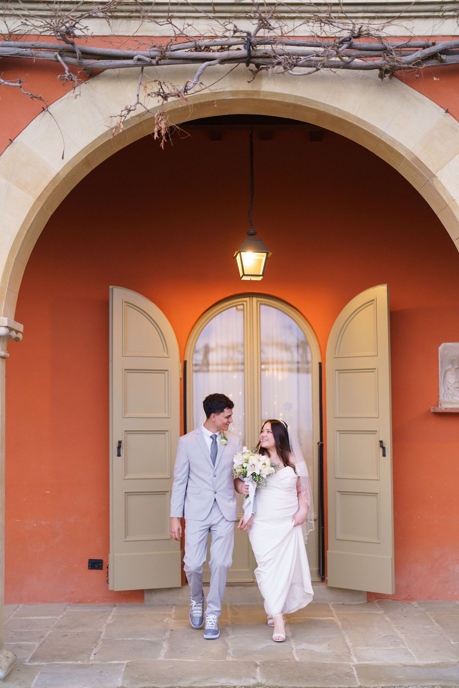 Couple in white and grey attire photographed under a series of terracotta-colored archways.