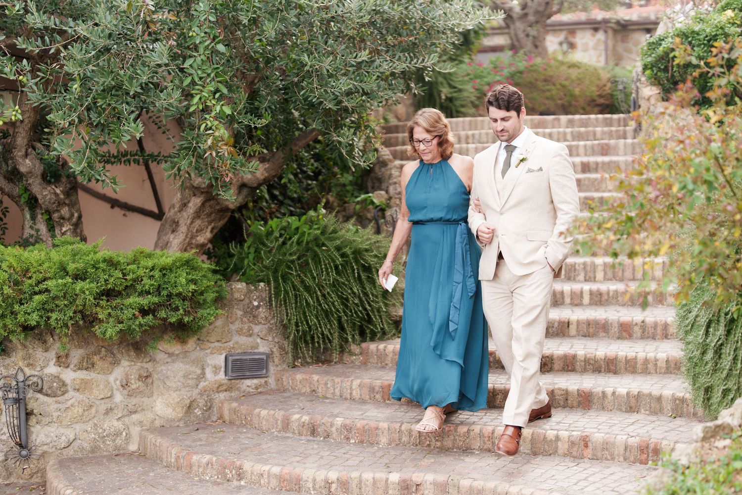 Couple in teal and white attire descending rustic brick stairs in a garden setting.