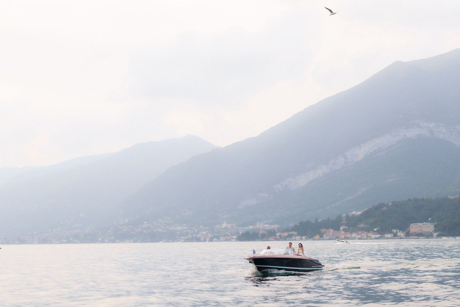 A speedboat creates a wake while cruising across calm waters with misty mountains visible in the background.