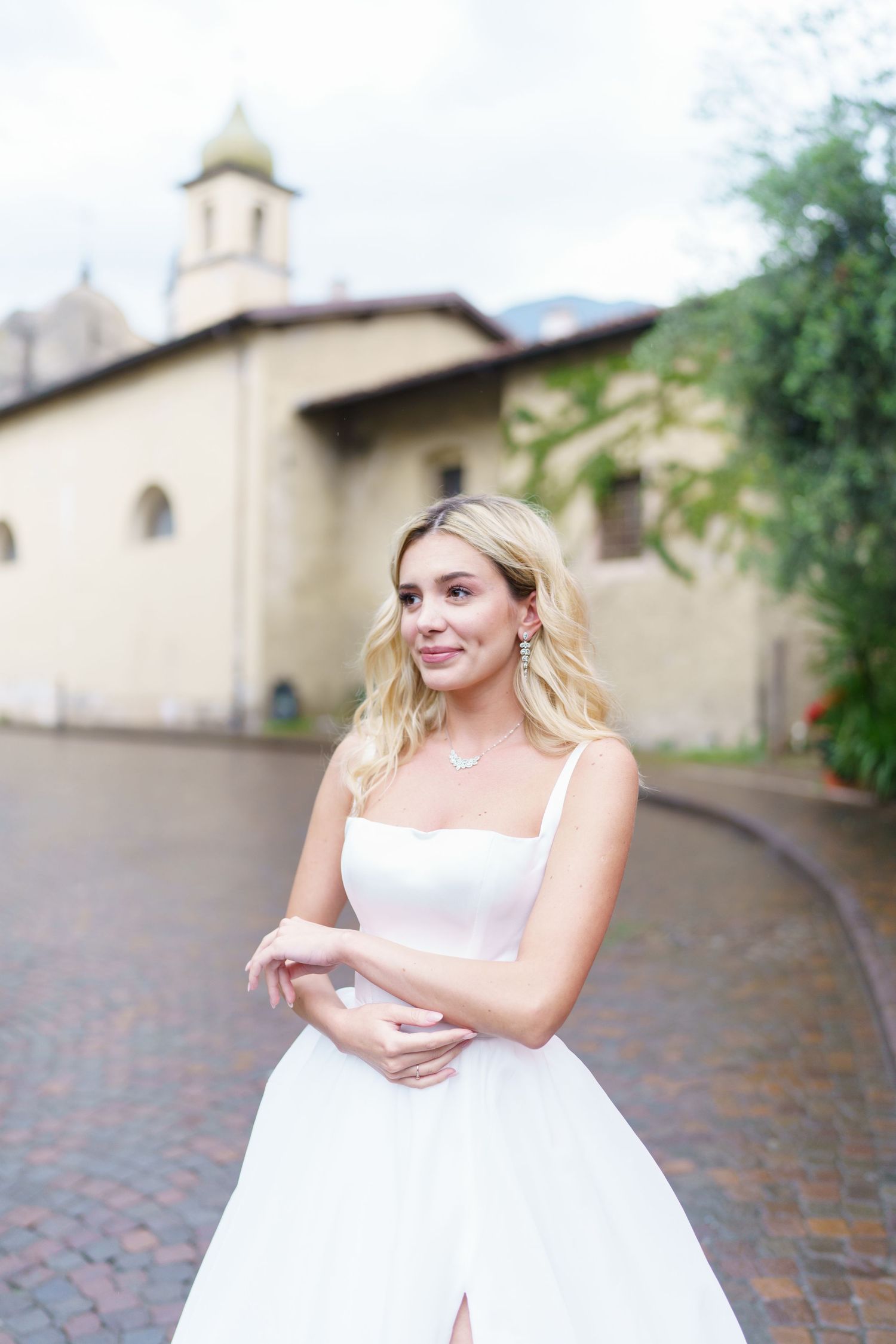 A bride in a white wedding gown poses on a curved brick walkway with a church building in the background.