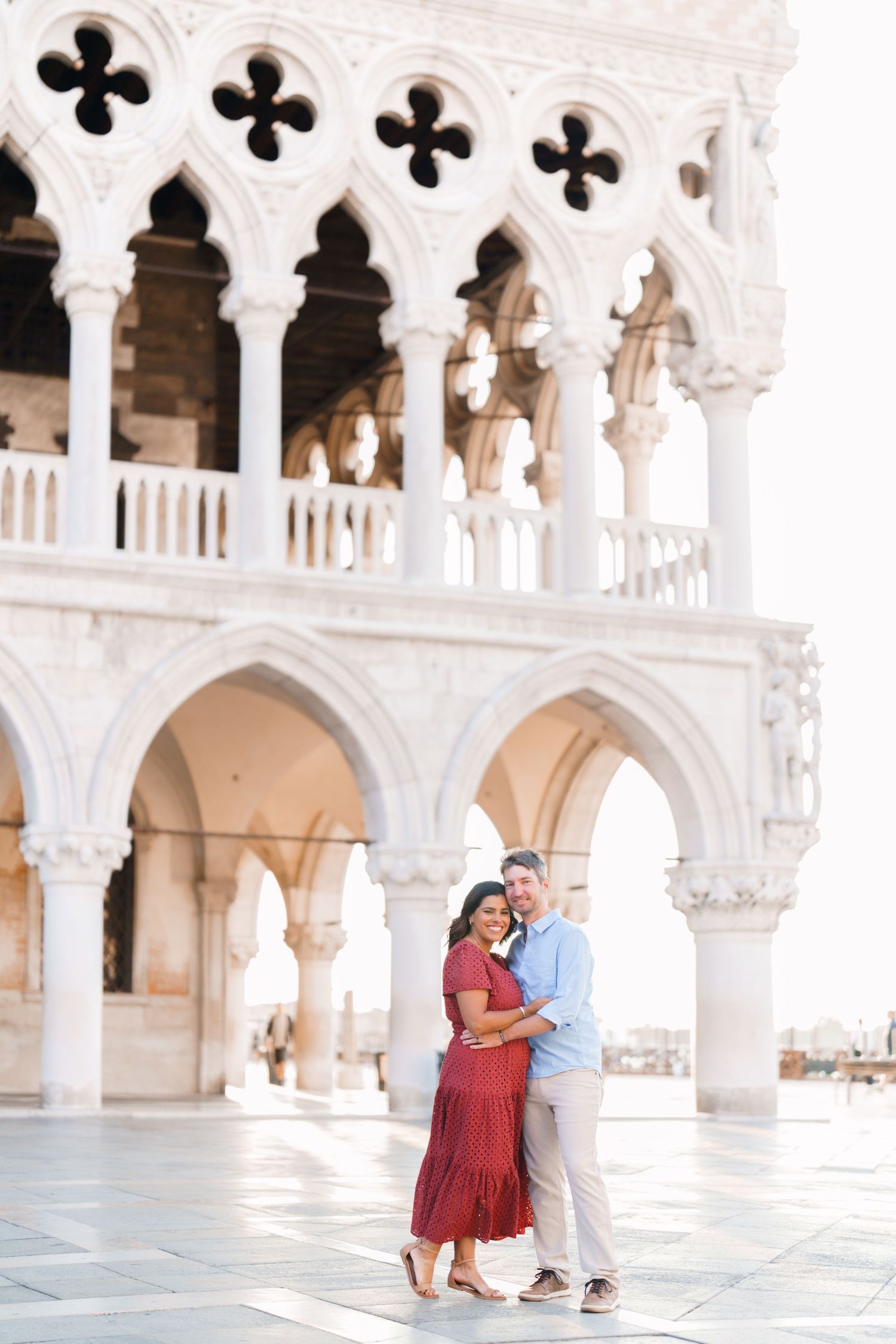Couple embracing in front of the ornate Gothic arches of the Doge's Palace in Venice, Italy.
