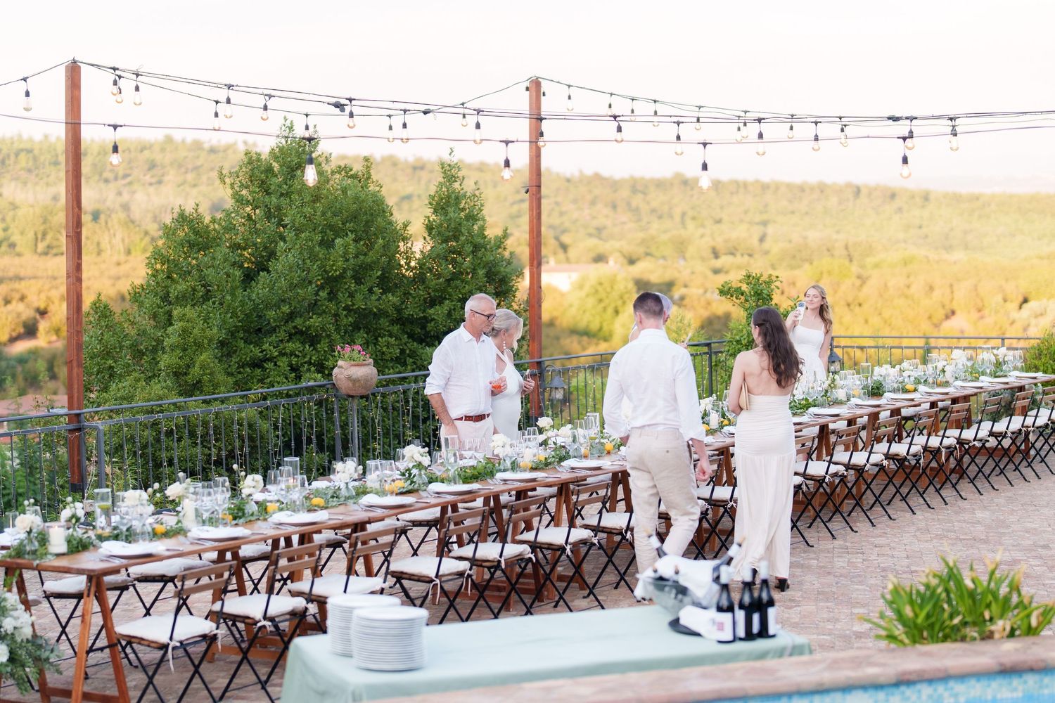 Elegant outdoor wedding reception with long tables, string lights, and scenic views at golden hour.