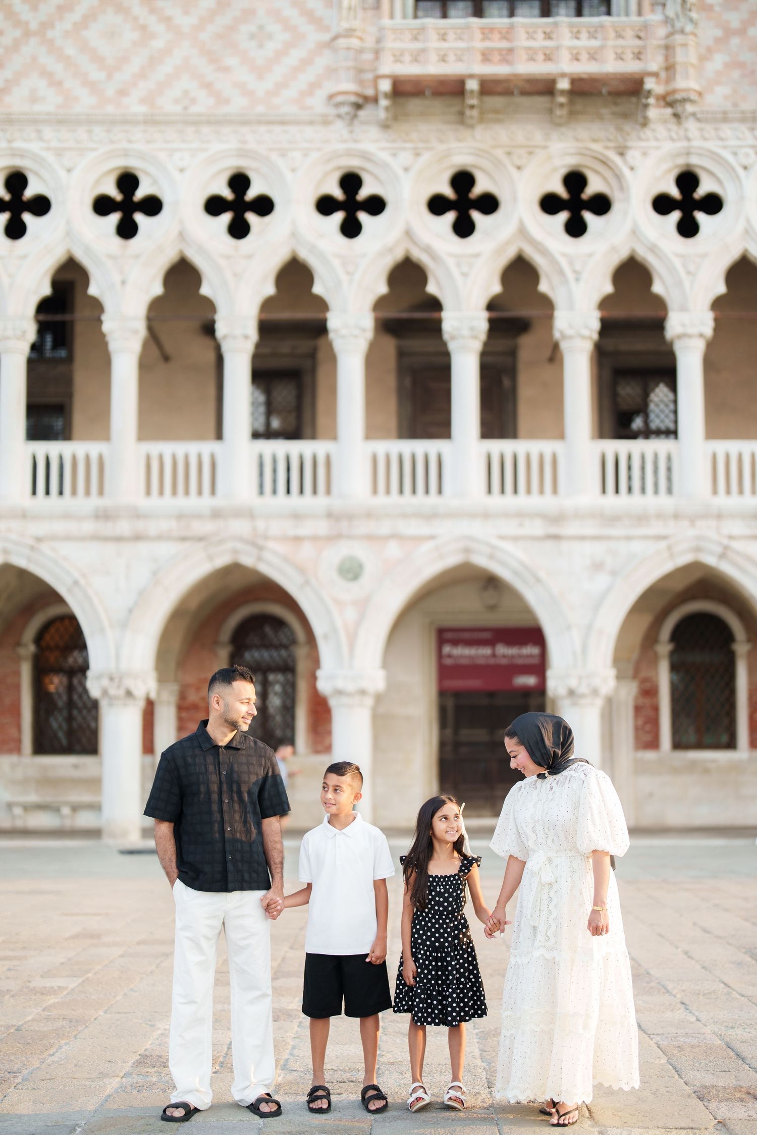Family of four holding hands in front of the ornate Doge's Palace in Venice, Italy.