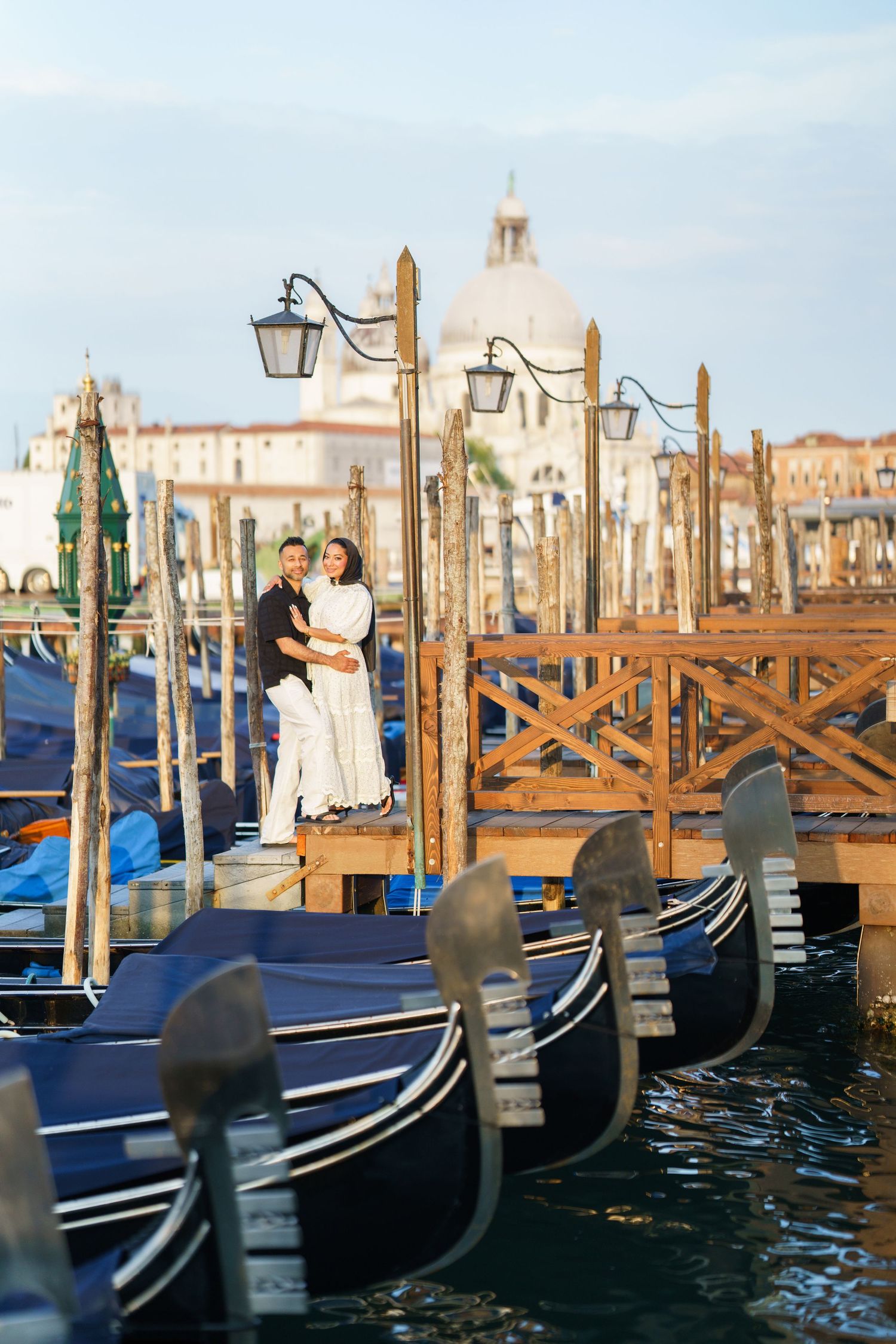 Romantic couple embracing on Venice gondola dock with Santa Maria della Salute basilica in background.