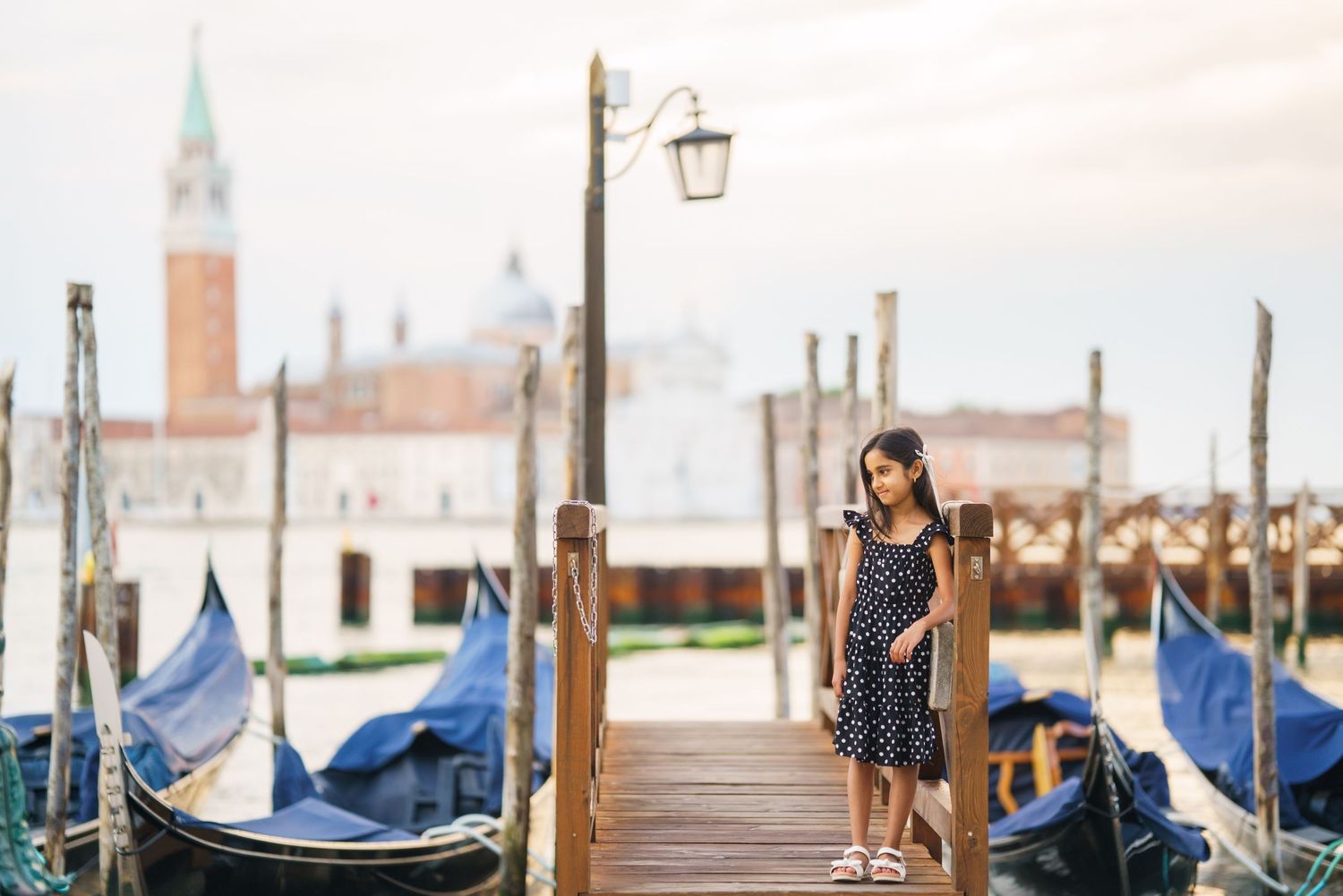 Young woman in polka dot dress standing on a wooden gondola dock in Venice, Italy, with San Giorgio Maggiore in background.