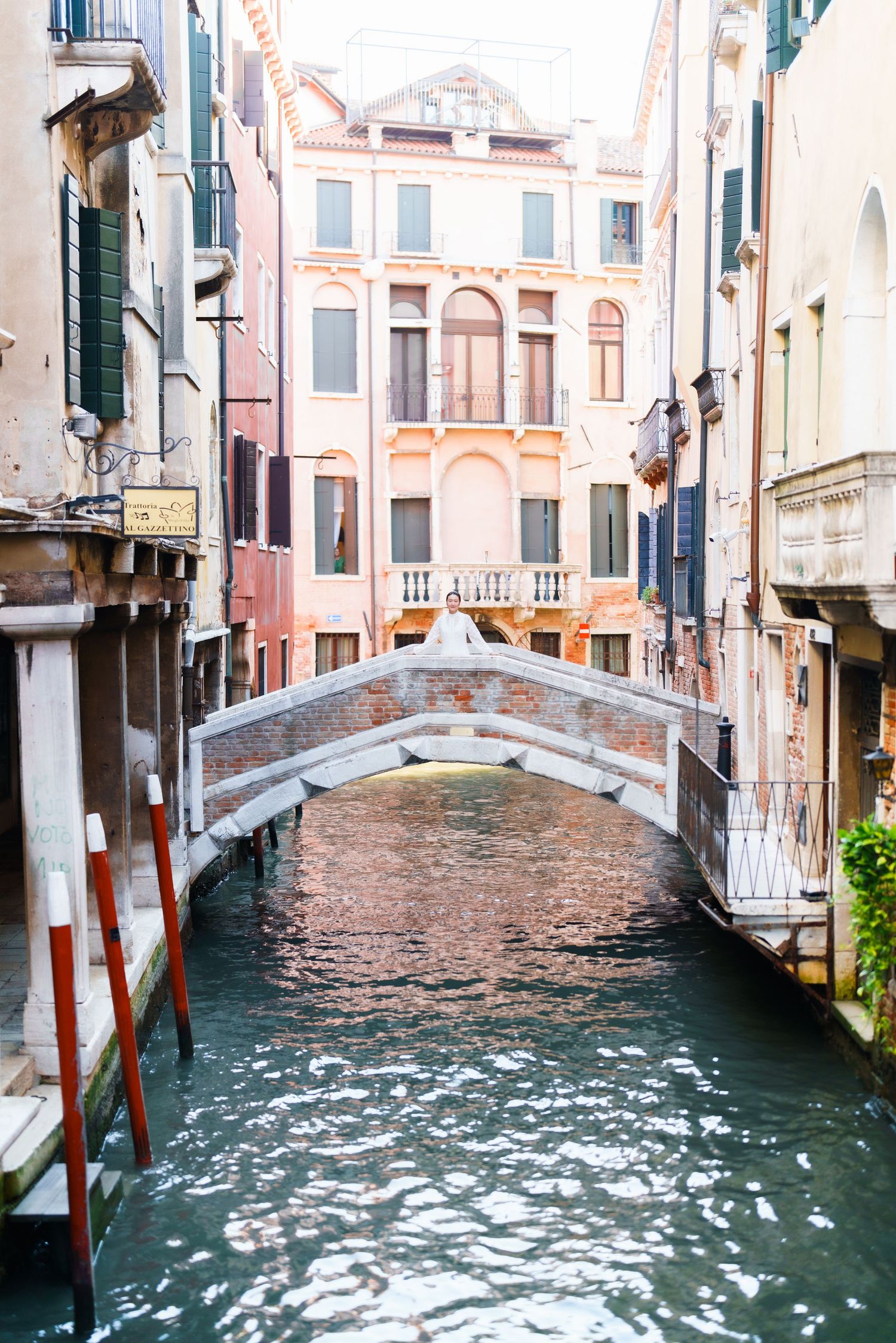 A narrow Venice canal with a historic brick bridge connecting colorful Renaissance buildings on a calm day.