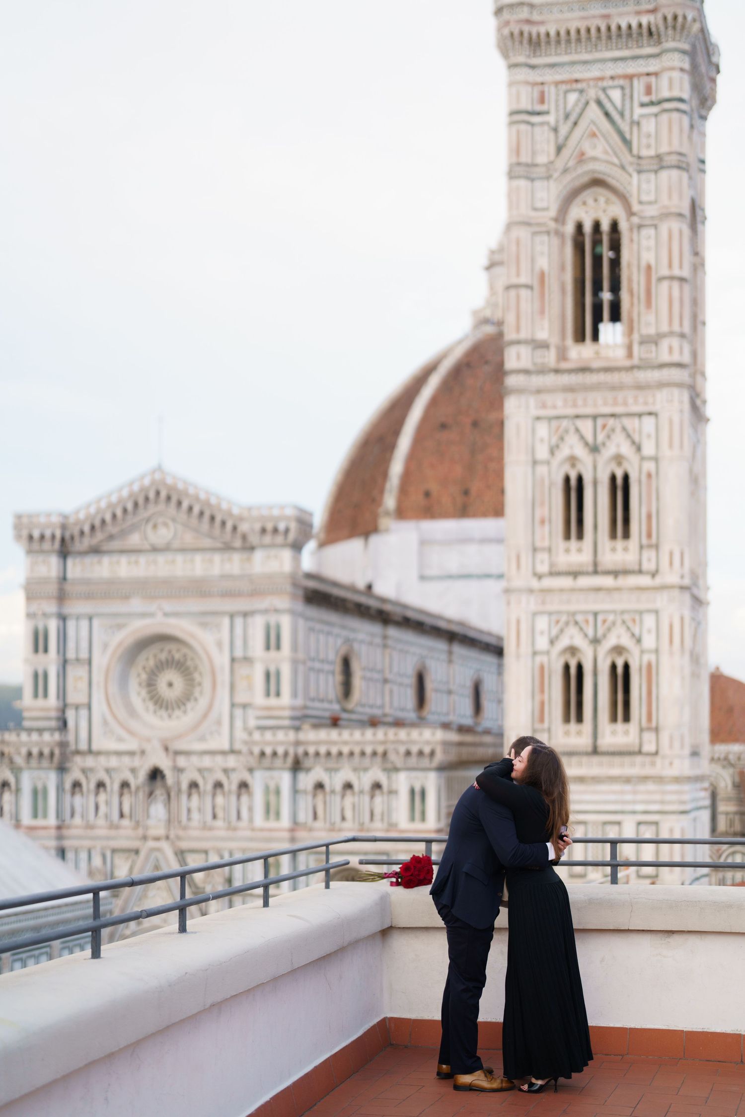 Couple embraces on terrace overlooking Florence Cathedral and Giotto's Bell Tower in Italy during romantic moment.
