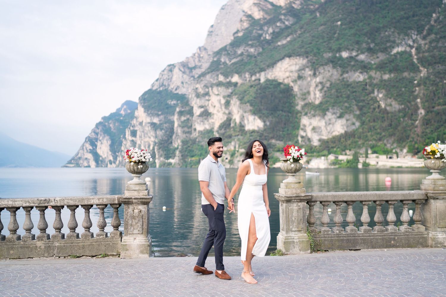 Couple enjoying a romantic moment on a lakeside terrace with stunning mountain views in Italy.