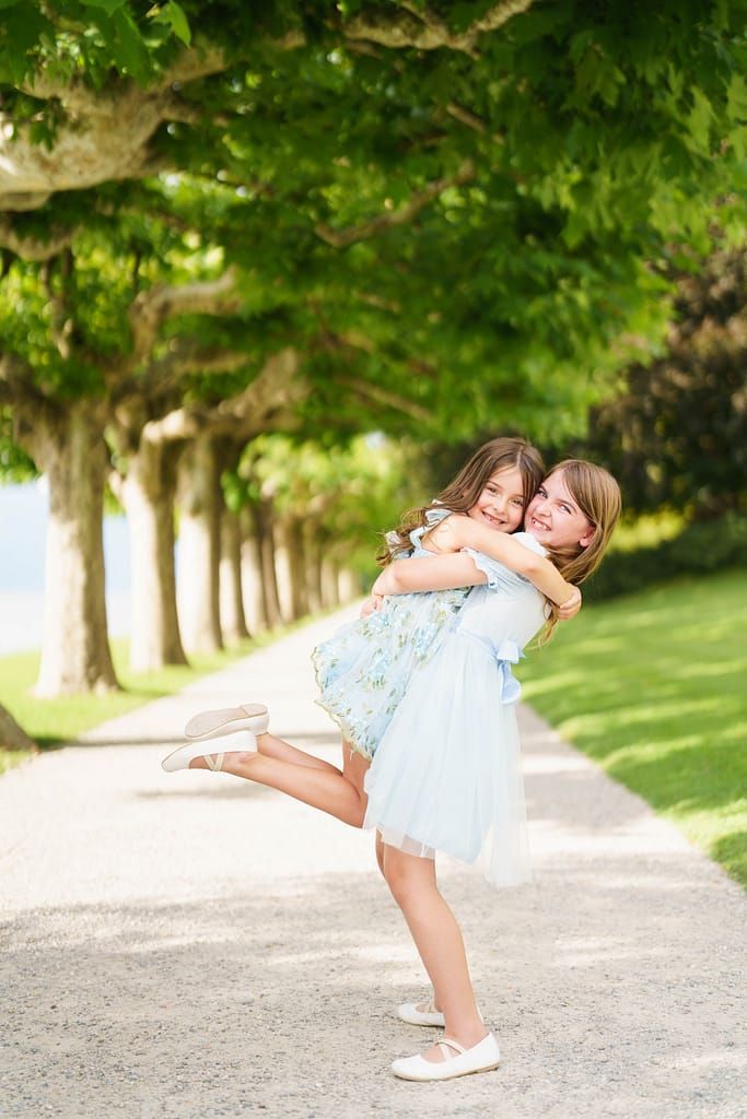 A tender embrace between two people in matching blue and white outfits along a tree-lined path on a sunny day.