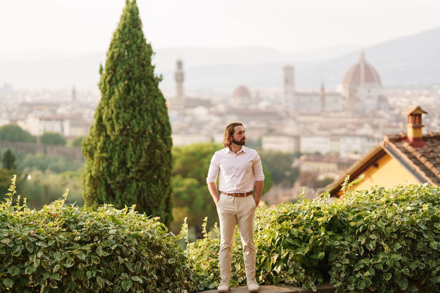 A couple shares a romantic moment overlooking a scenic city view from a hilltop garden terrace.