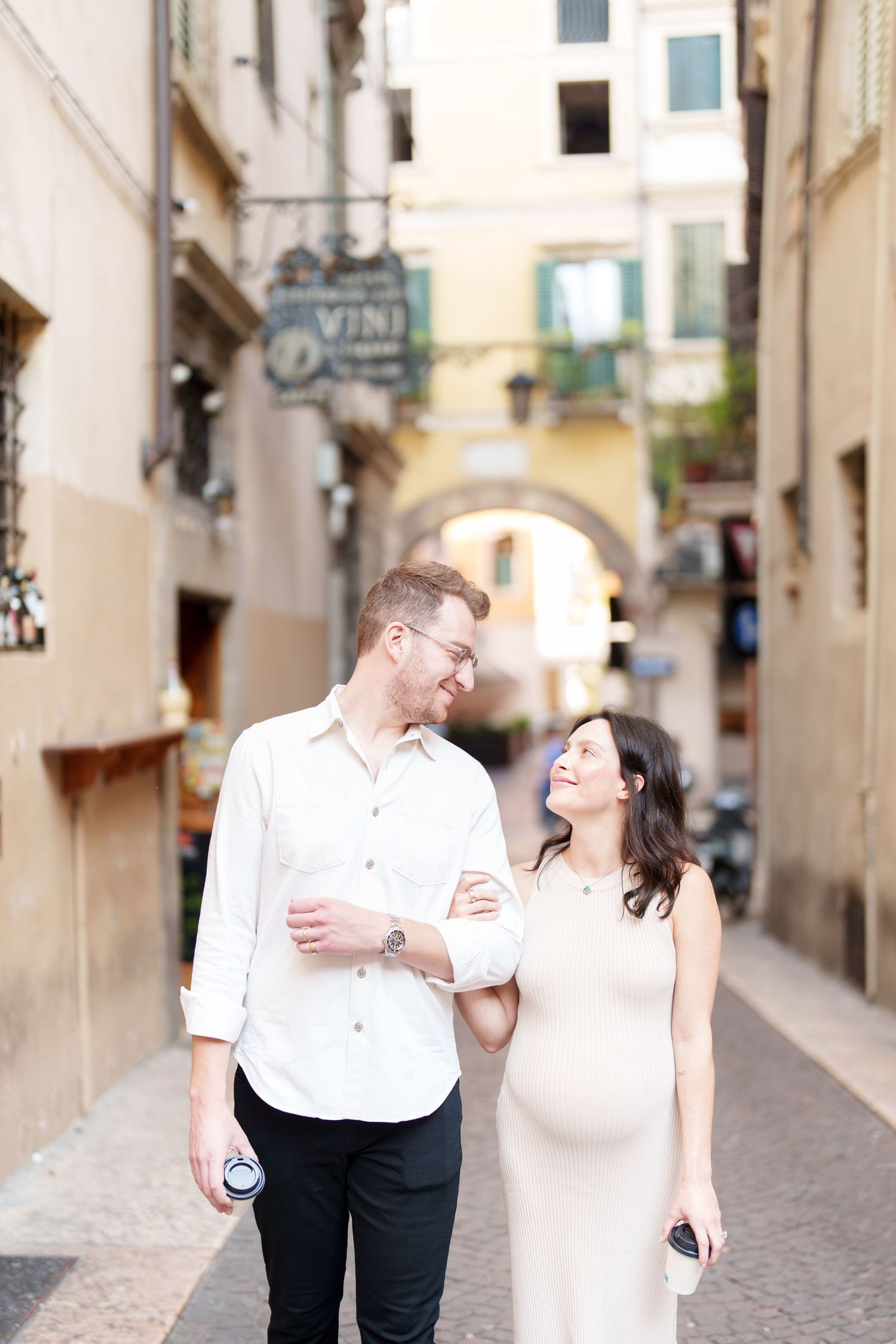 A romantic couple shares joyful moments while walking through charming European cobblestone streets.