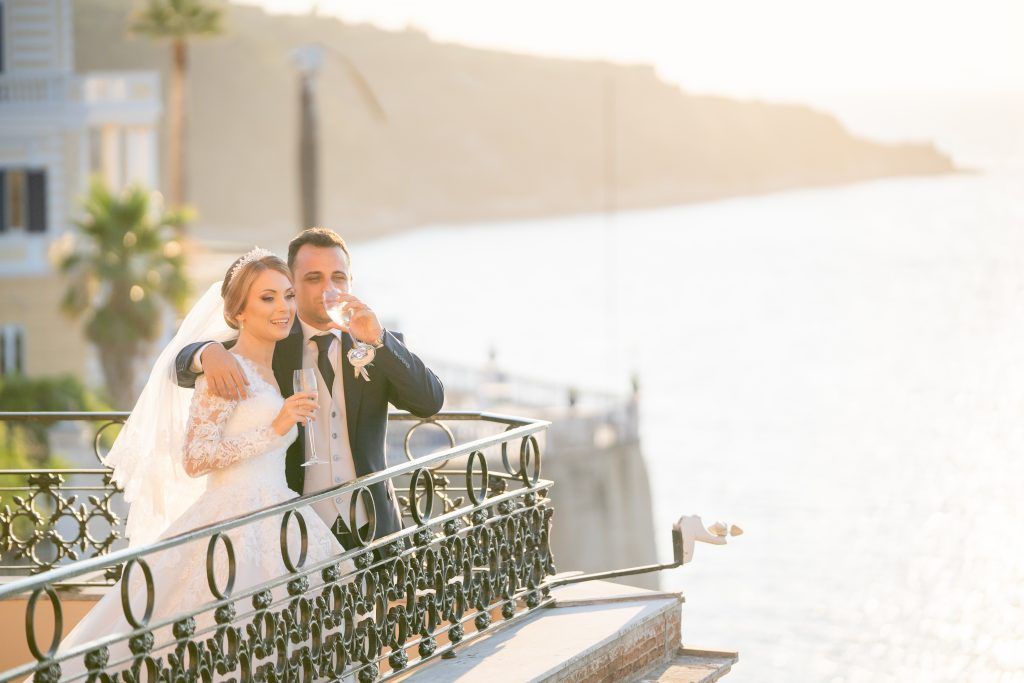 Romantic outdoor wedding scene with sunlit balcony and decorative railings.