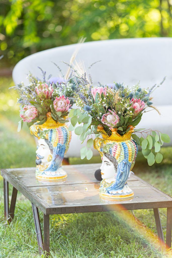 Decorative ceramic vases with floral arrangements displayed on metal tables in an outdoor garden setting.