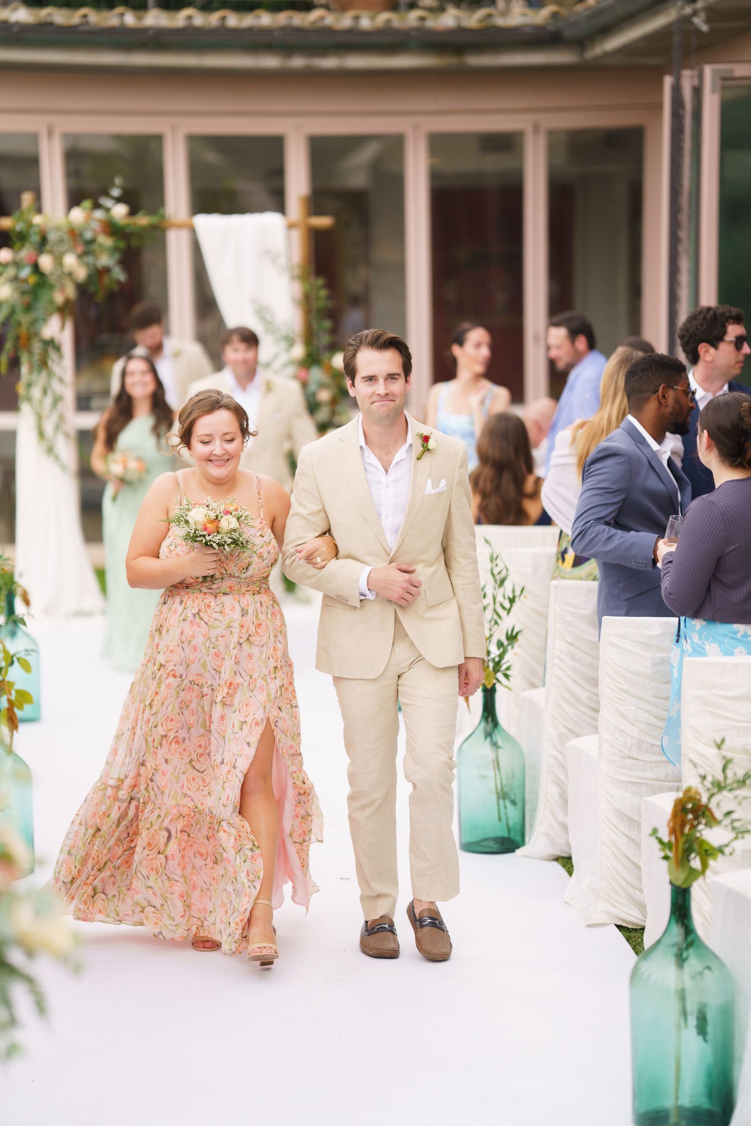 Wedding reception guests mingling at an outdoor venue with floral decorations and turquoise glass vases.