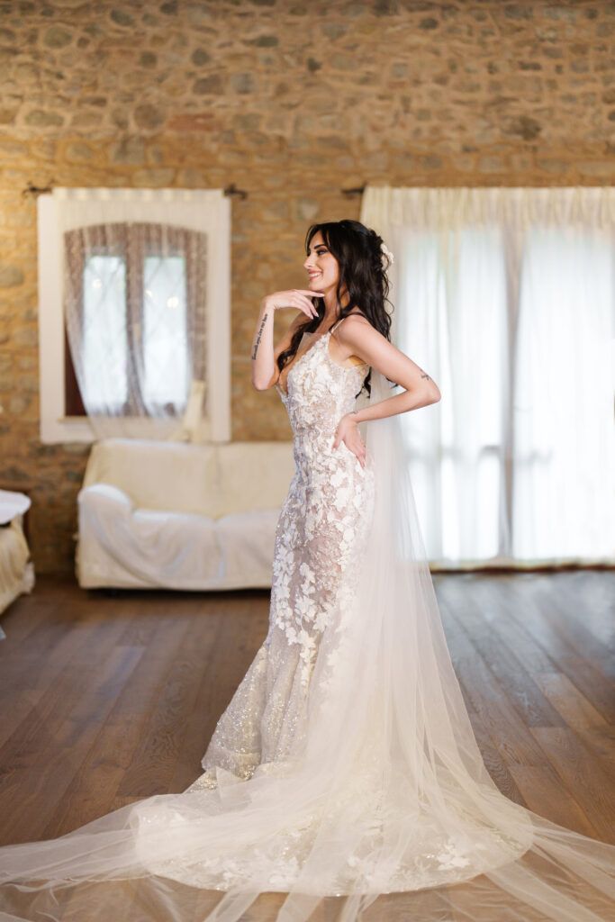 A stunning lace wedding dress with a flowing train displayed in a rustic stone-walled room with wooden floors.