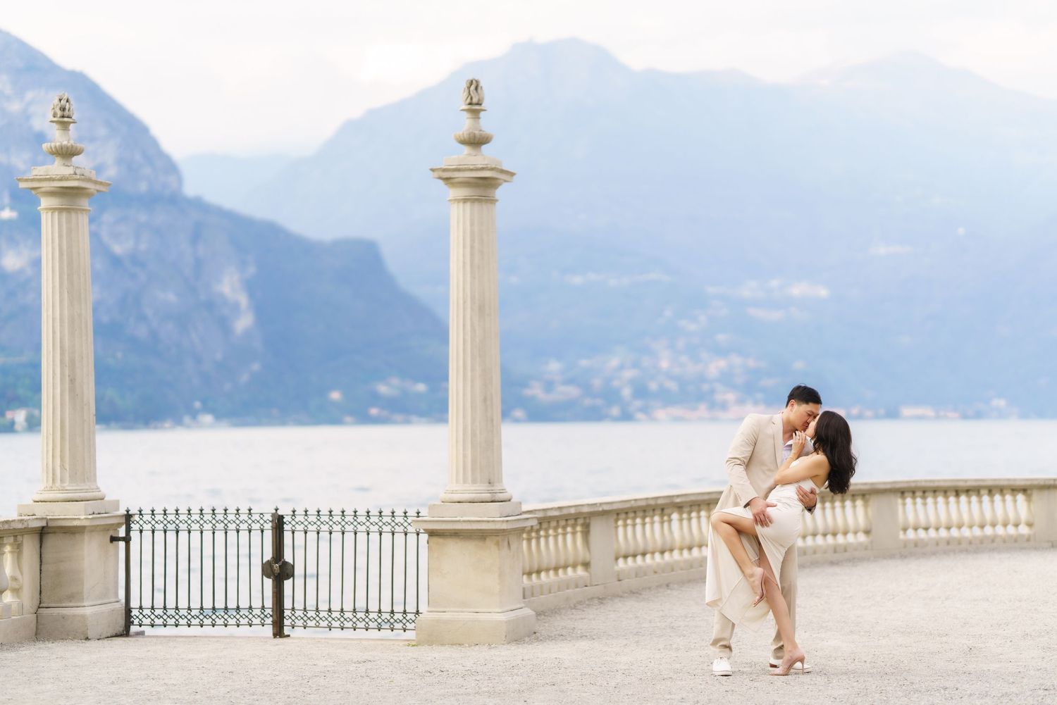 Romantic couple embraces on an elegant white terrace overlooking a scenic mountain coastline.