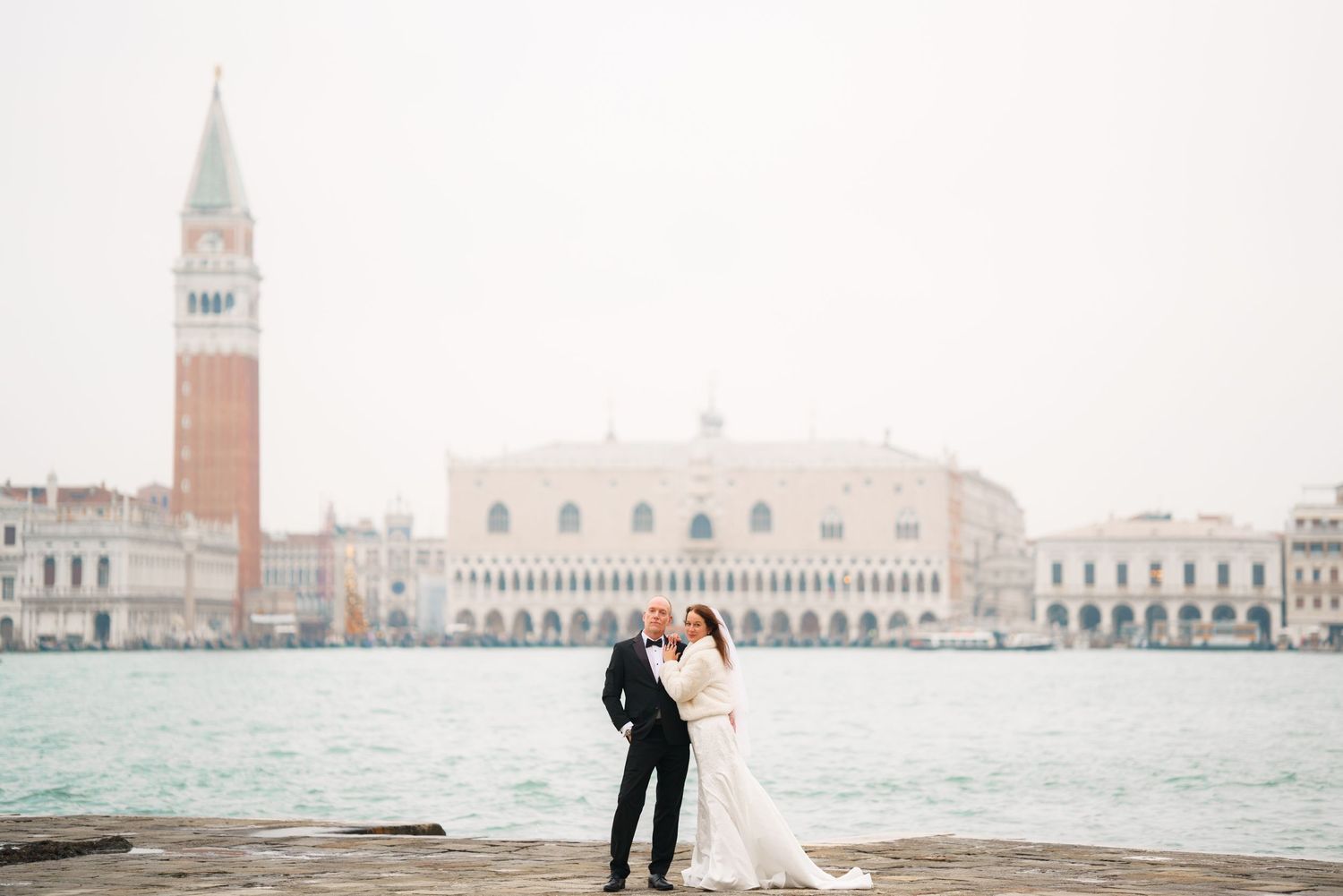 A couple embraces in front of the iconic St Mark's Square in Venice, Italy with the Grand Canal in the background.