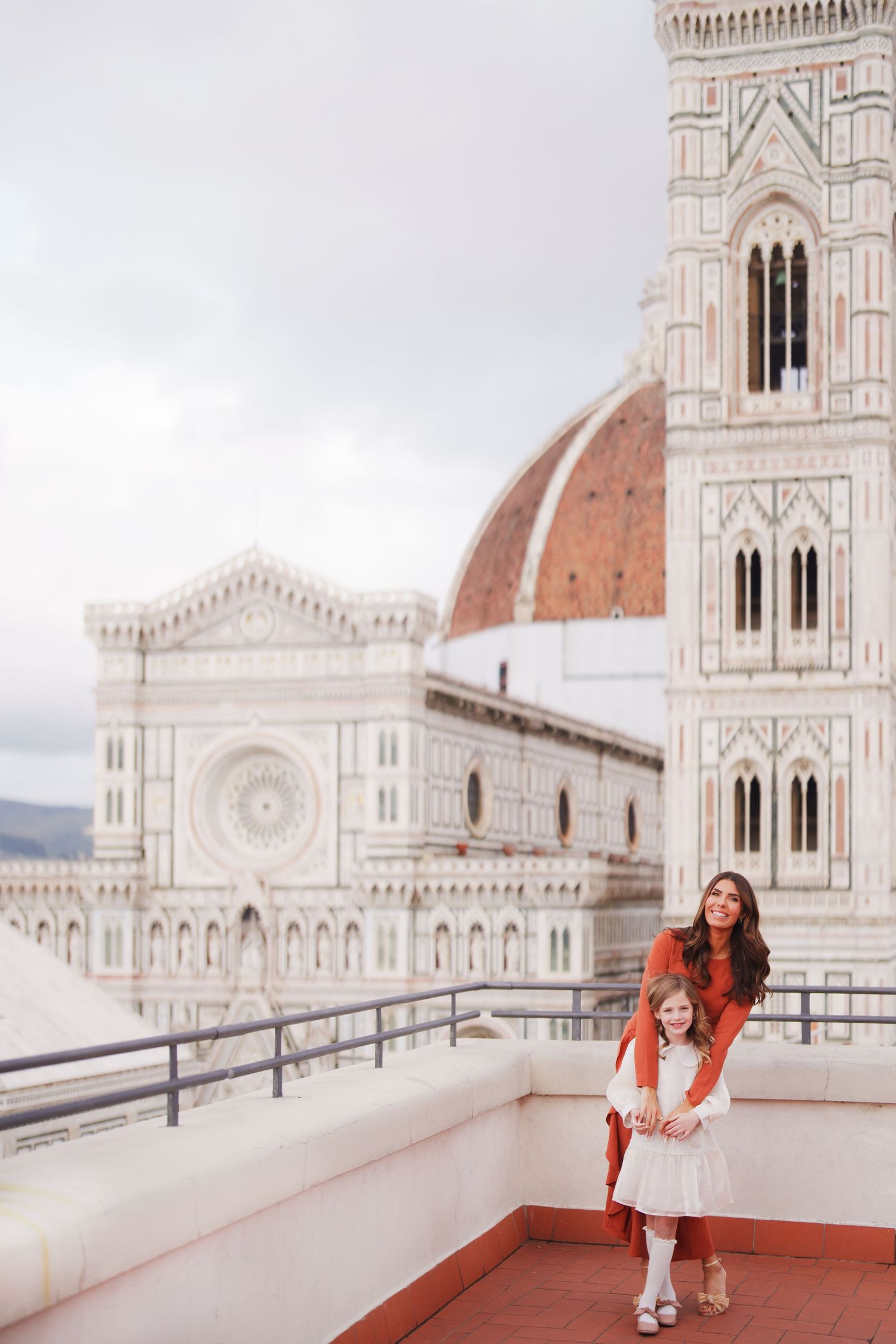 Mother and daughter posing on a rooftop terrace with Florence Cathedral and Giotto's Campanile in Italy.