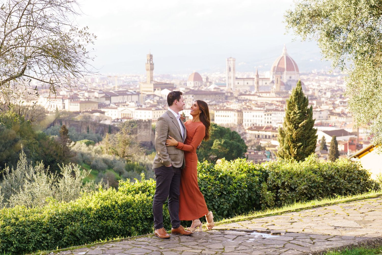 Couple embracing with Florence skyline, Duomo cathedral and cityscape visible behind them on a sunny day.