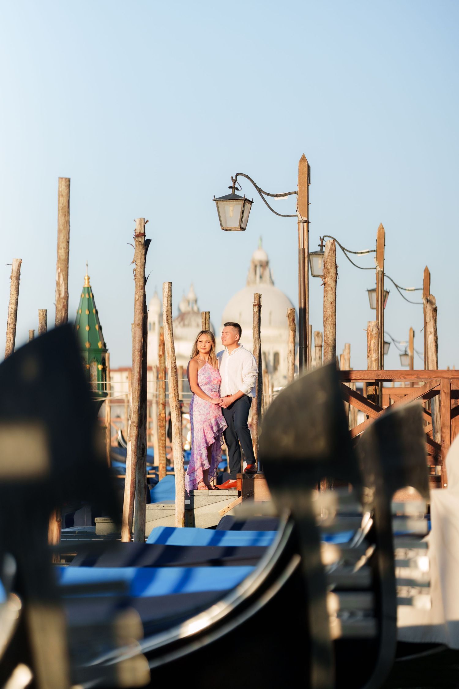 Romantic couple embracing on Venice gondola dock with Santa Maria della Salute church in background.