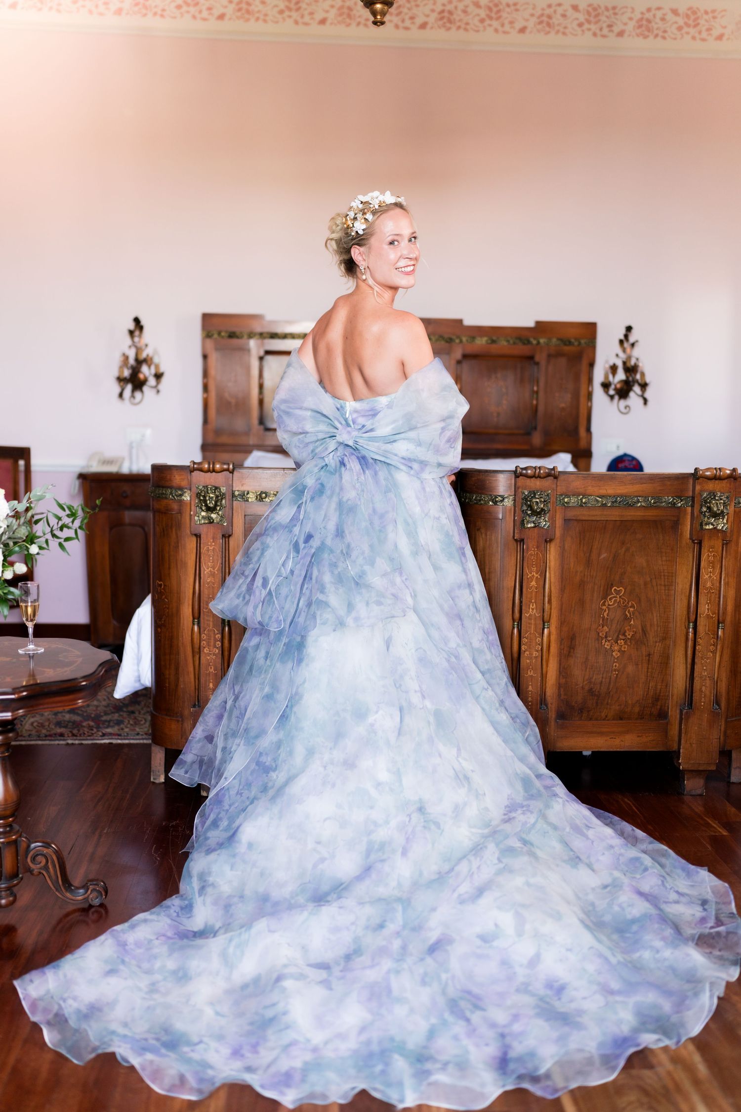 Bride in a stunning blue floral watercolor ball gown with bow, posing in an elegant wood-paneled room.