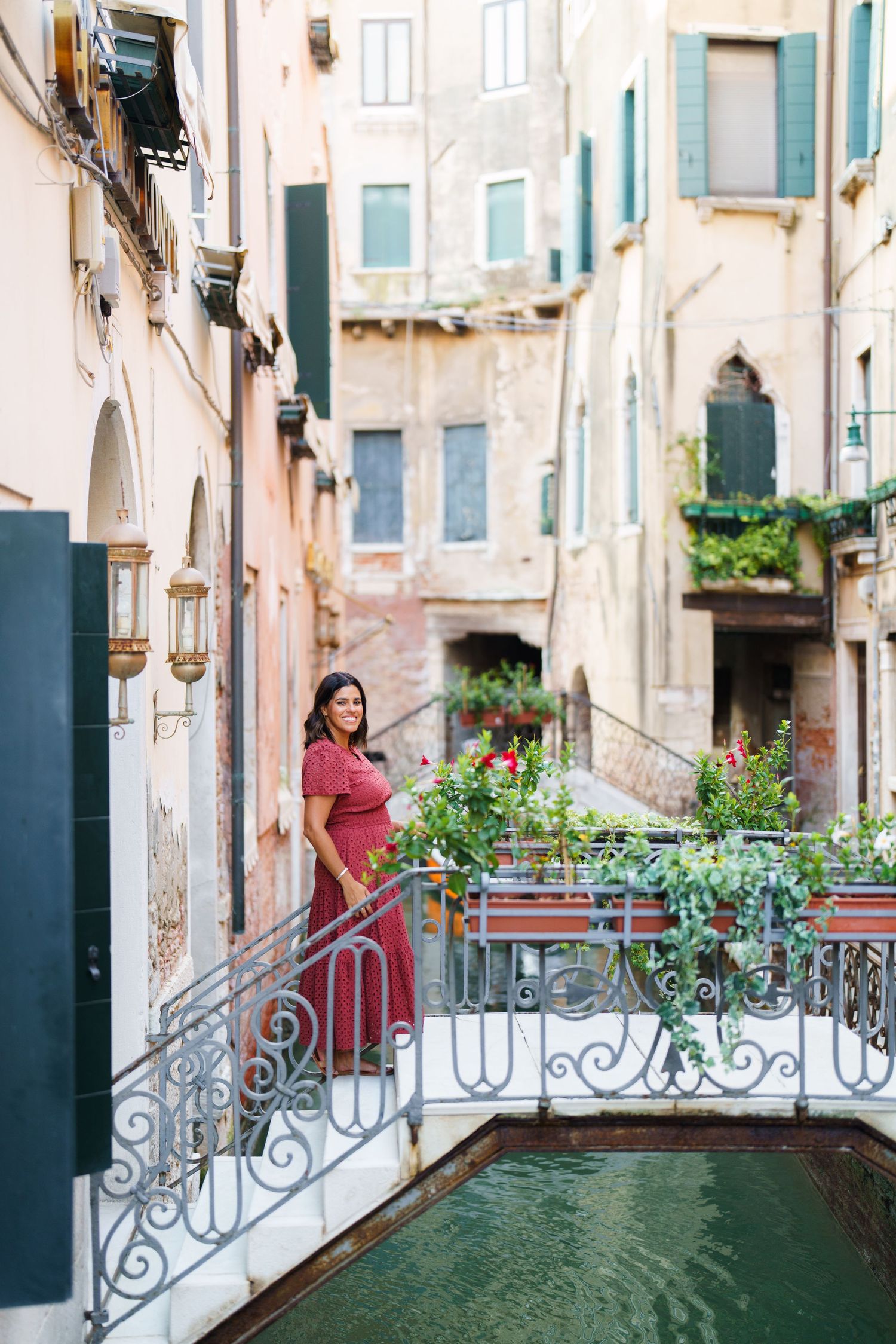 Woman in red dress standing on ornate bridge over canal in Venice, Italy, surrounded by historic buildings.