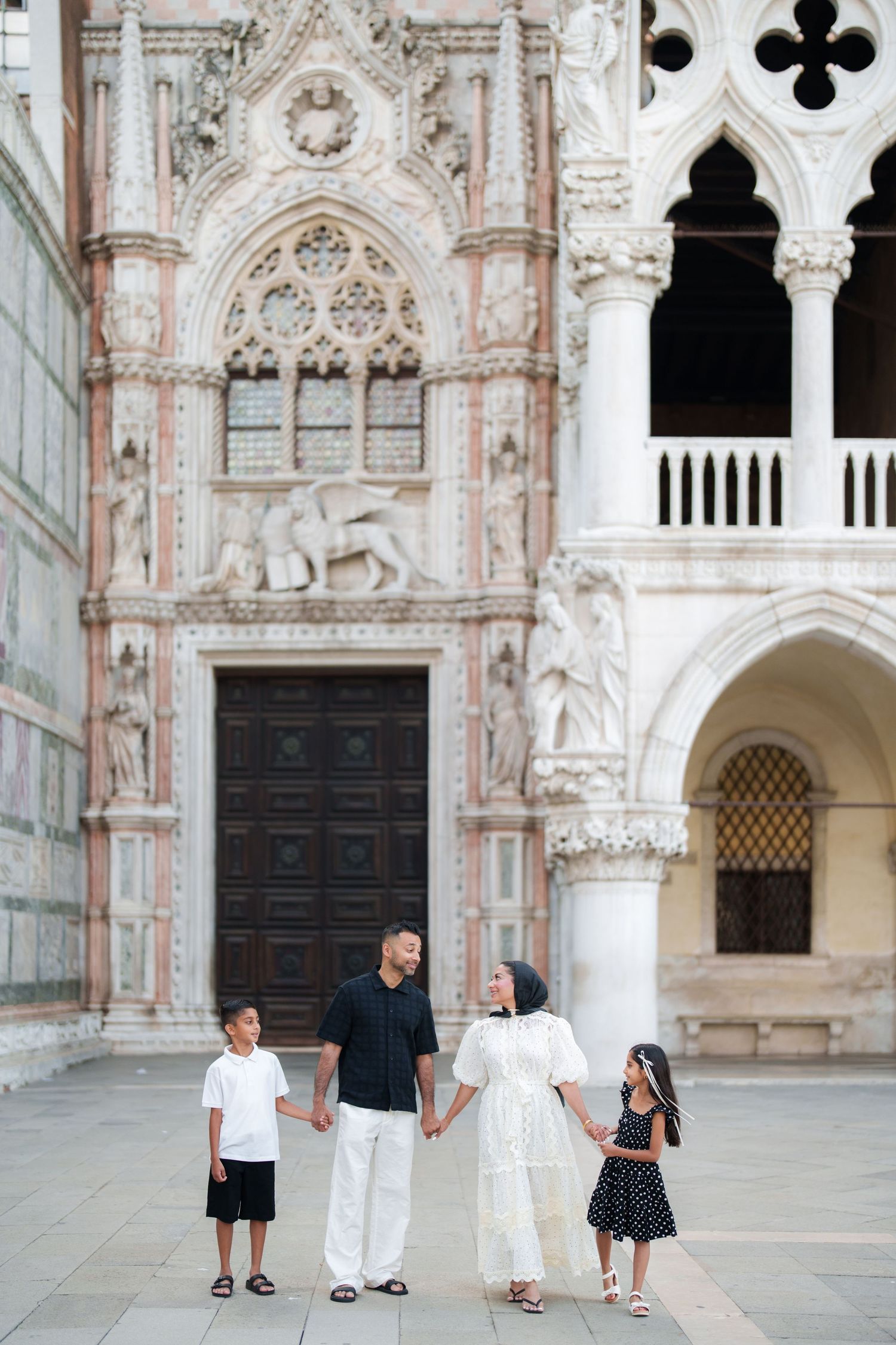 Family of four holding hands in front of ornate Venetian architecture at Doge's Palace, Venice, Italy.