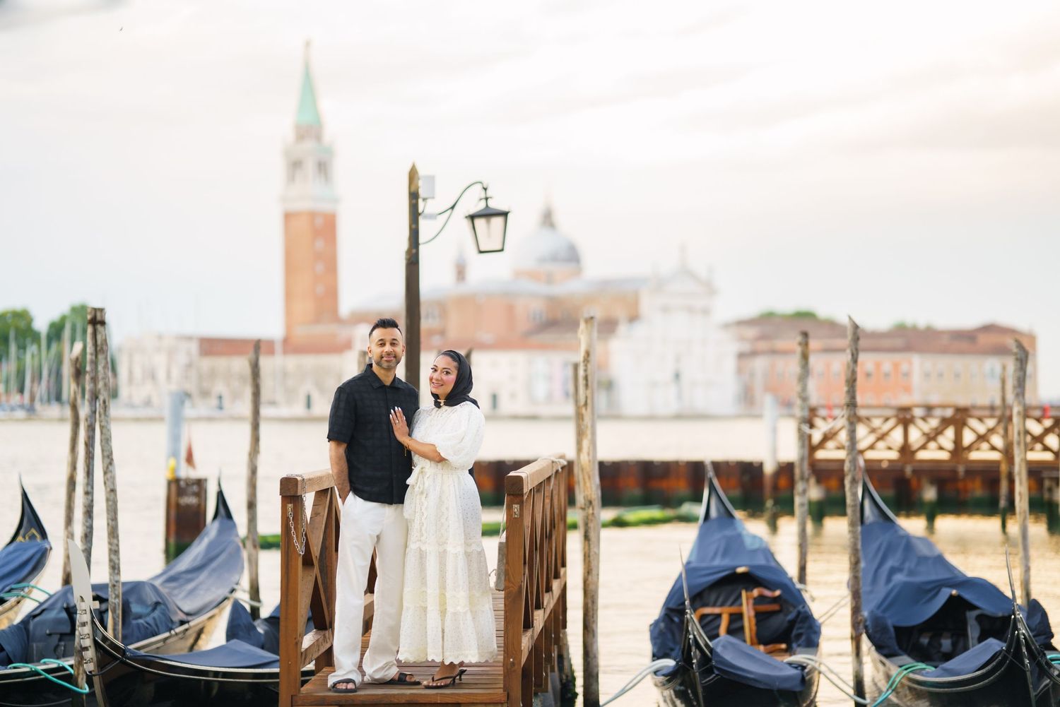 Couple embracing on a Venice dock with gondolas and San Giorgio Maggiore island in the background.