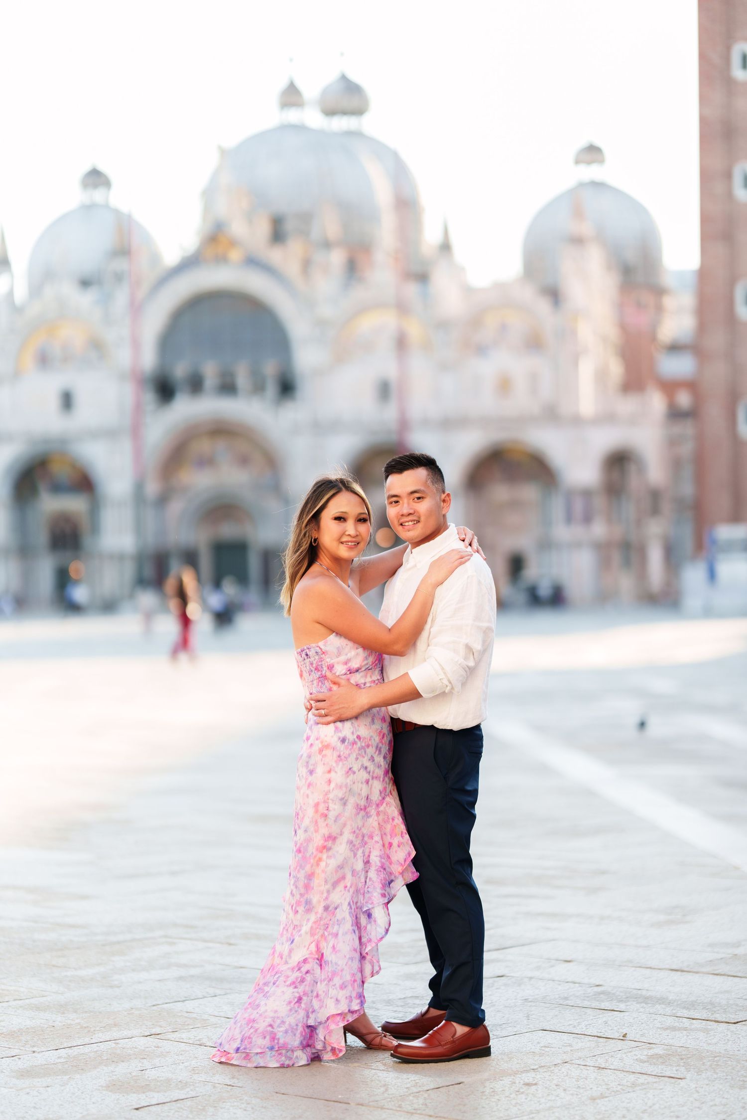 Couple embracing in Piazza San Marco, Venice, with St. Mark's Basilica in the background at golden hour.