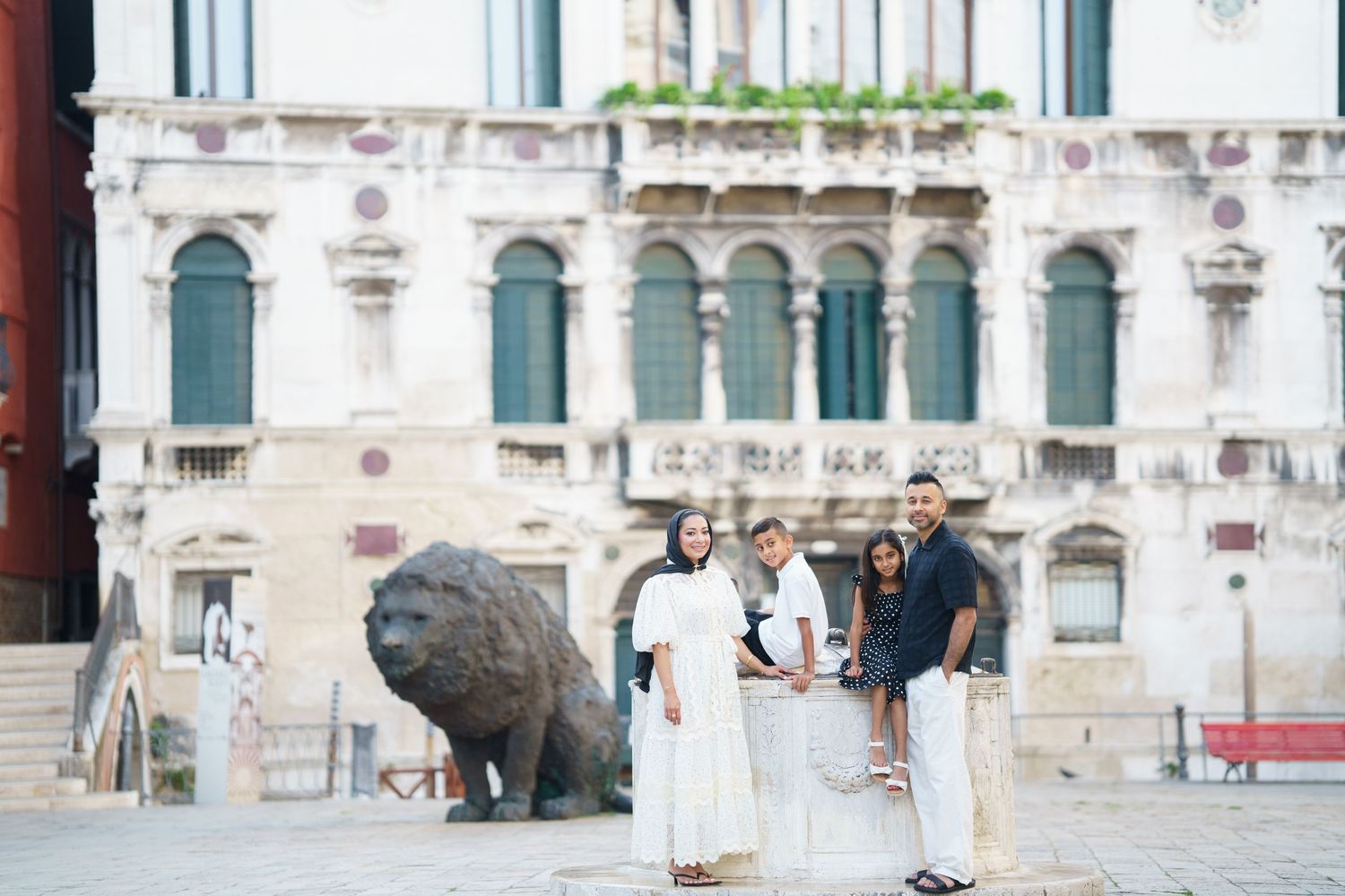 Family of three posing in front of a historic Venetian palace with a bronze lion sculpture in Venice, Italy.