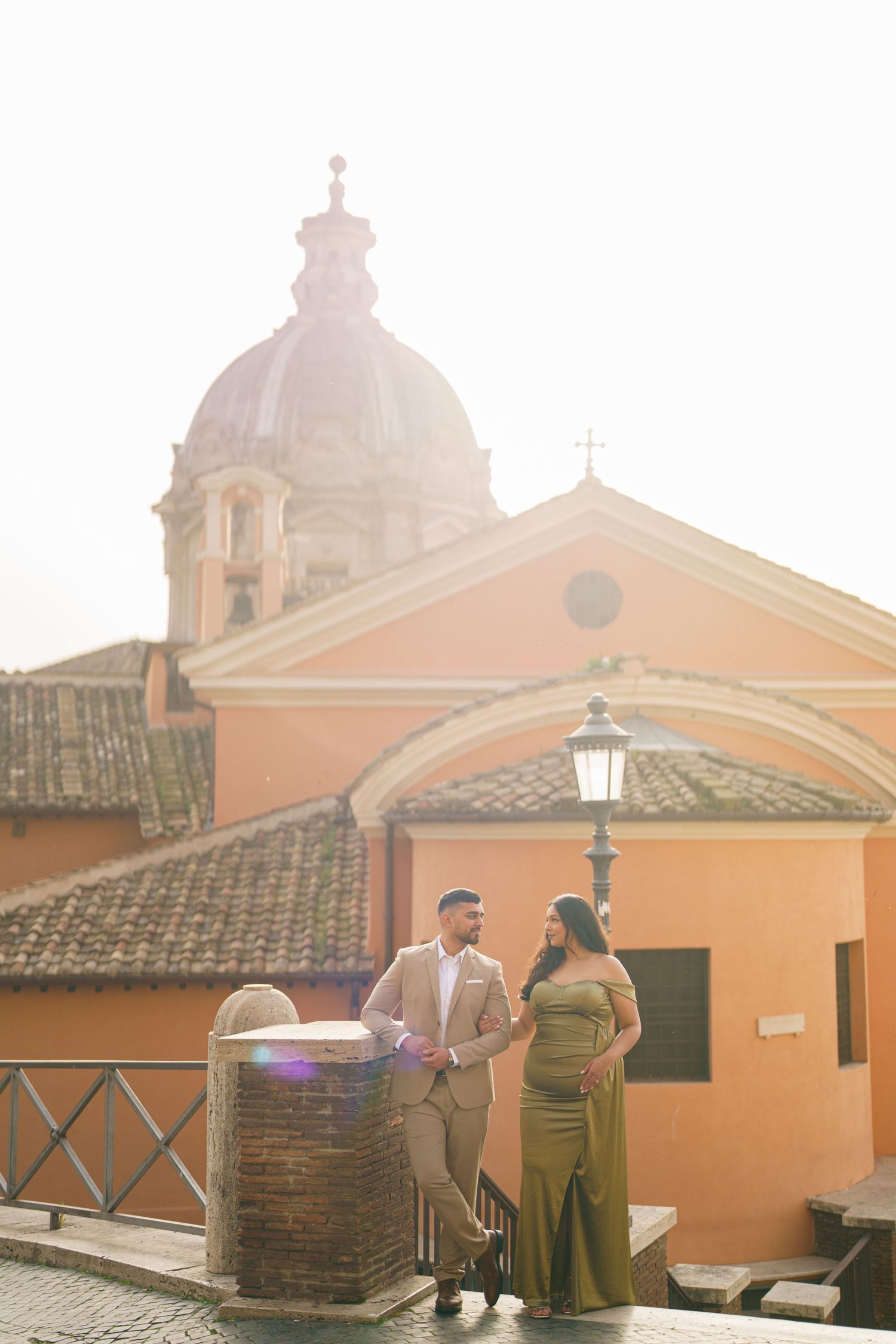 Couple posing in front of a Roman church dome and orange buildings at golden hour in Rome, Italy.