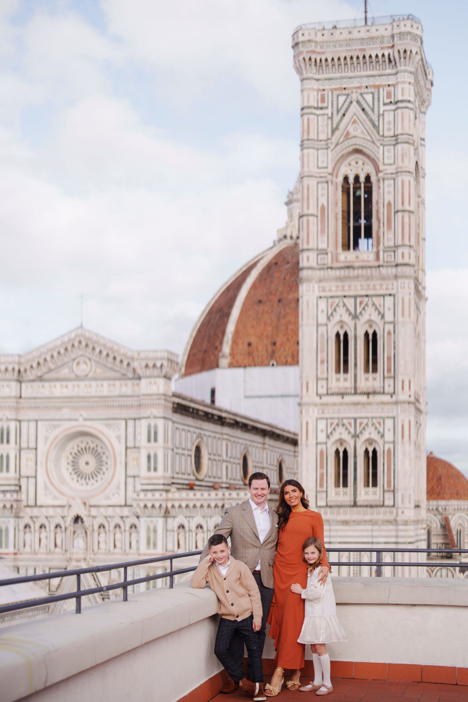Family posing on a rooftop terrace with Florence Cathedral and Giotto's Campanile in the background.