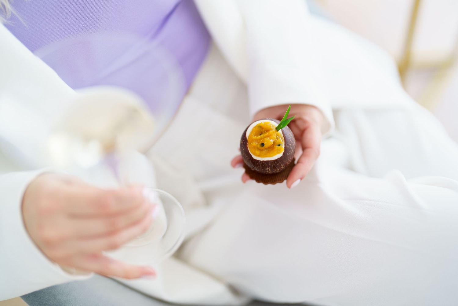 Person in white outfit holding a chocolate tart topped with passion fruit and a mint leaf.