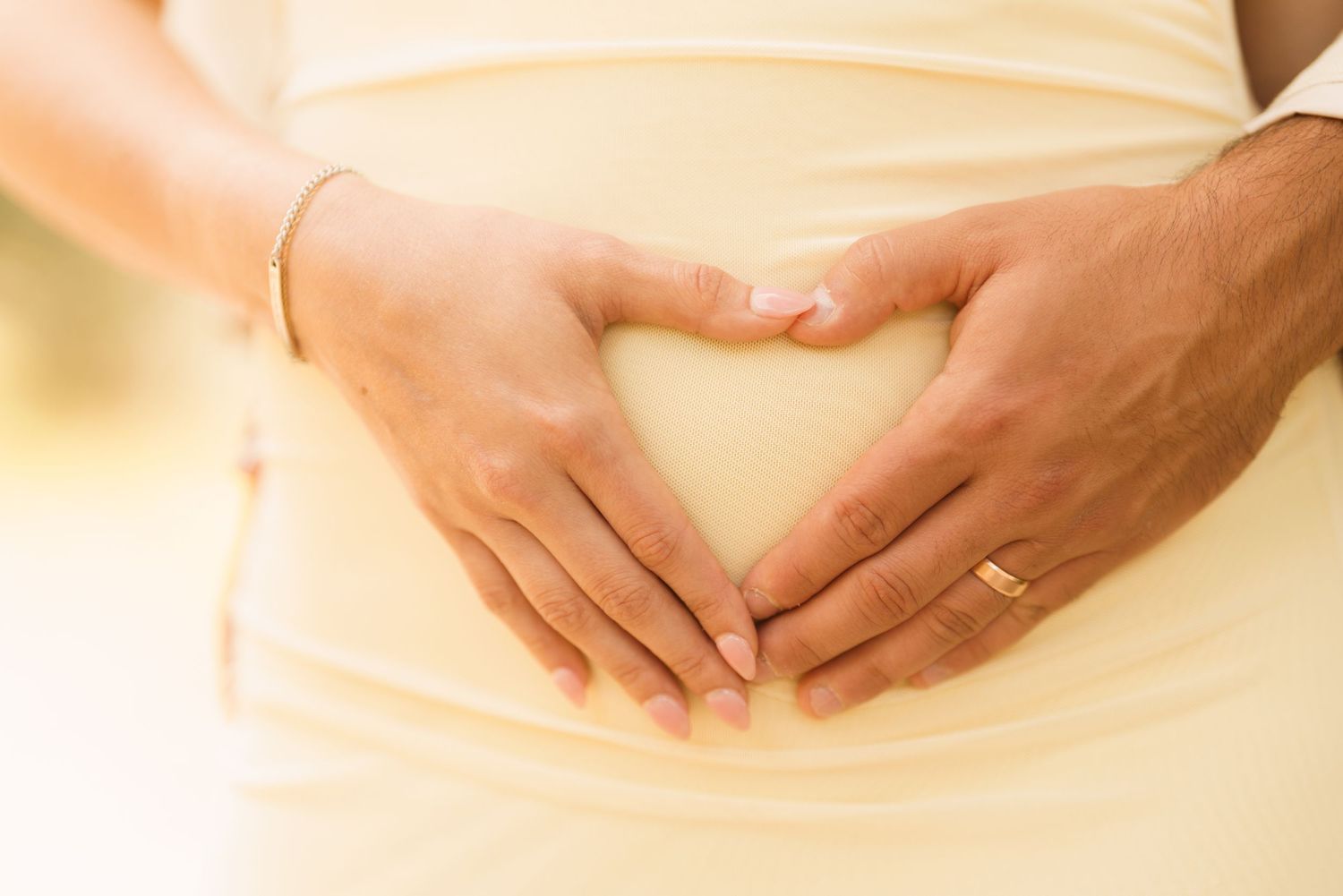Couple forming a heart shape with hands on pregnant belly, wearing wedding ring, maternity love concept.