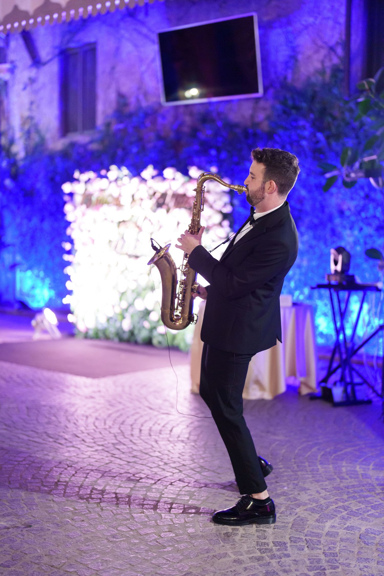 A performer in black formal attire dances energetically on a cobblestone floor under dramatic blue lighting.
