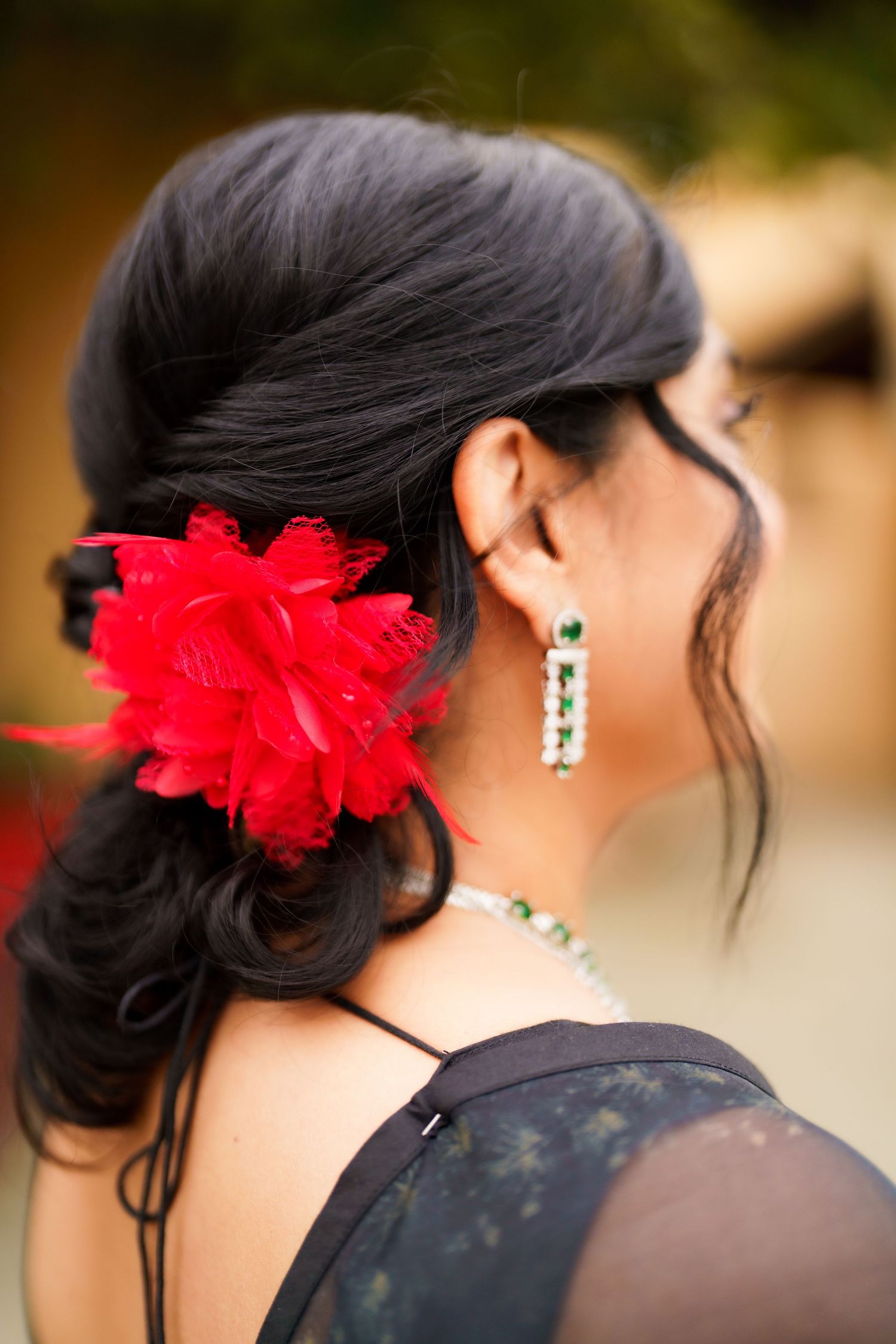 Close-up of dark hair adorned with vibrant red flower and dangling earrings.