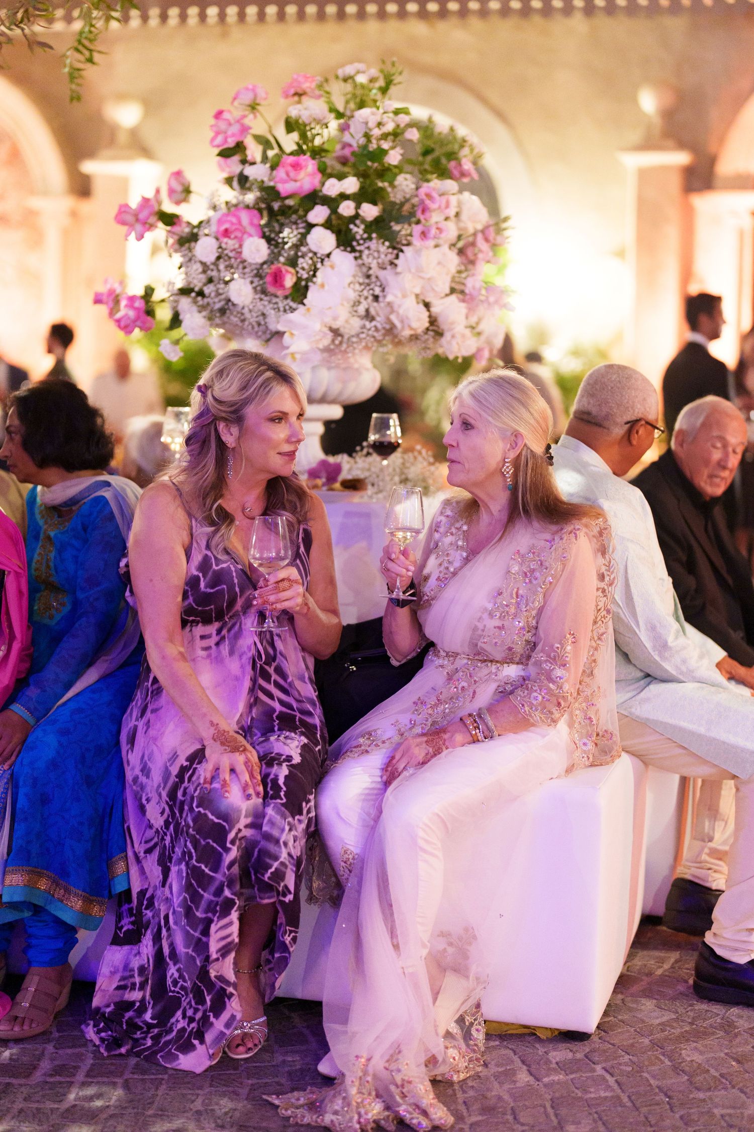 Wedding reception guests socializing at decorated tables with elaborate floral centerpieces.