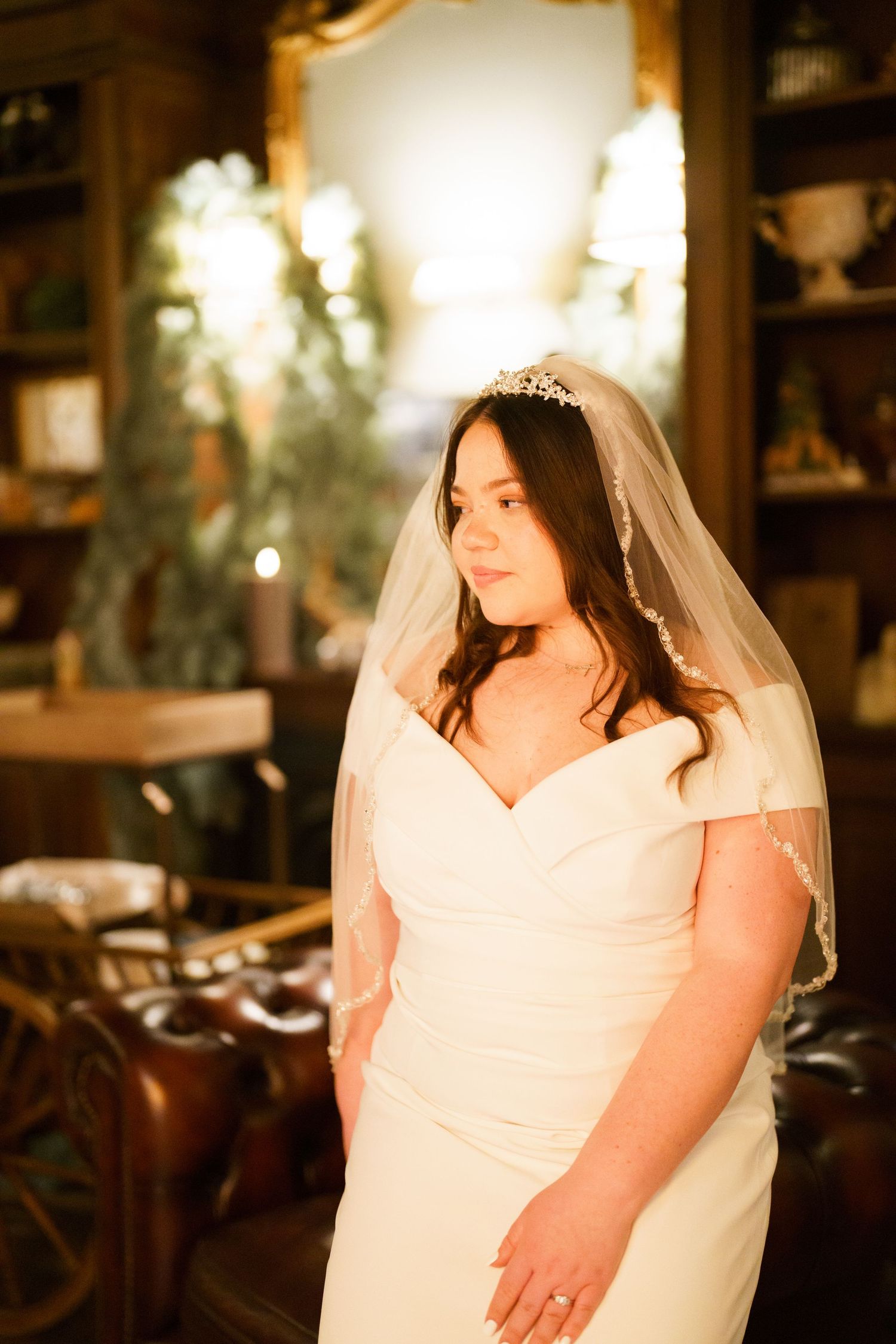 A bride in a white wedding dress and veil poses in a softly lit indoor setting.
