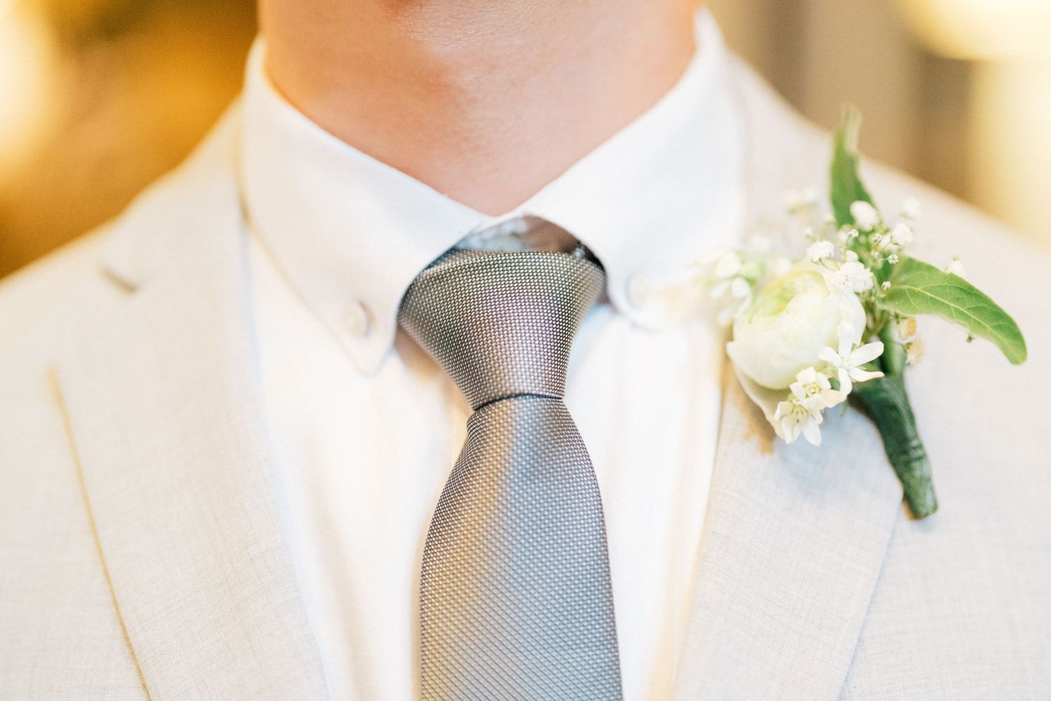 Close-up detail of white boutonniere and grey tie against formal attire.